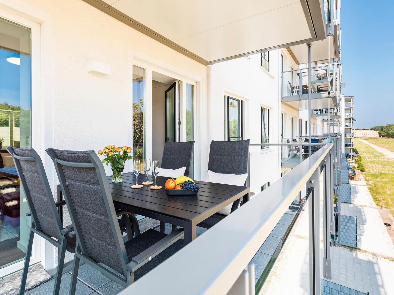 Terrasse mit Tisch, Stühlen und Obst. Blick auf Wohngebäude und Grünfläche.