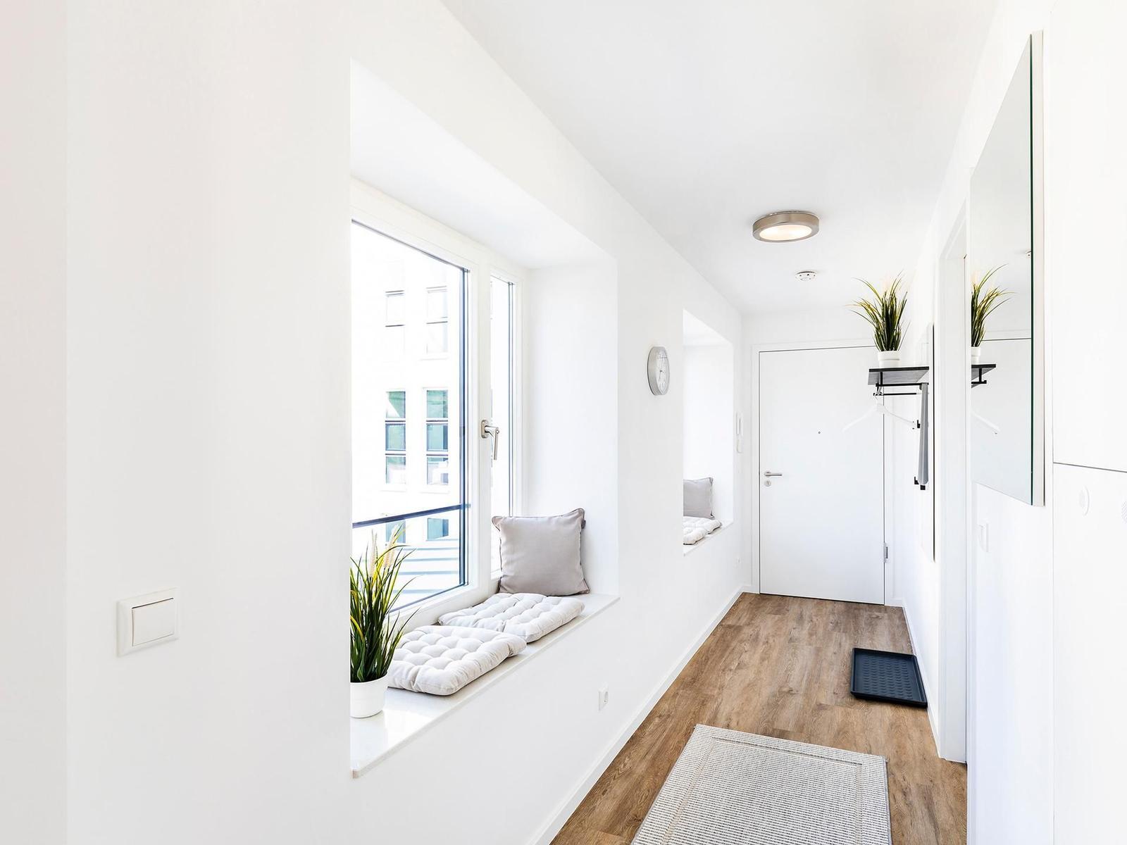 Hallenflur mit Fensterbank, Pflanzen und Holzboden. Tür und Spiegel sind sichtbar.