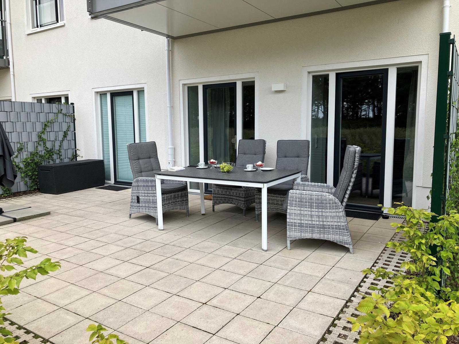 Terrasse mit Sitzgruppe, Tisch und Sonnenschutz vor Haus mit Glasfronten.