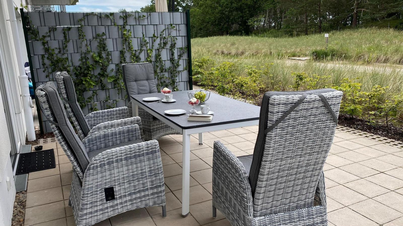 Terrasse mit Esstisch und Stühlen, Hintergrund mit Pflanzenwand und Grünflächen.