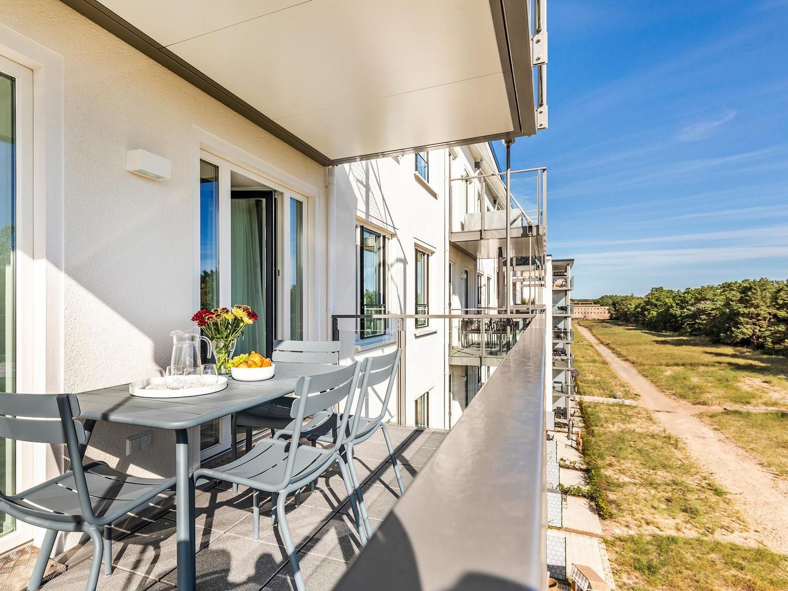 Terrasse mit Tisch, Stühlen und Blick auf Grünflächen.