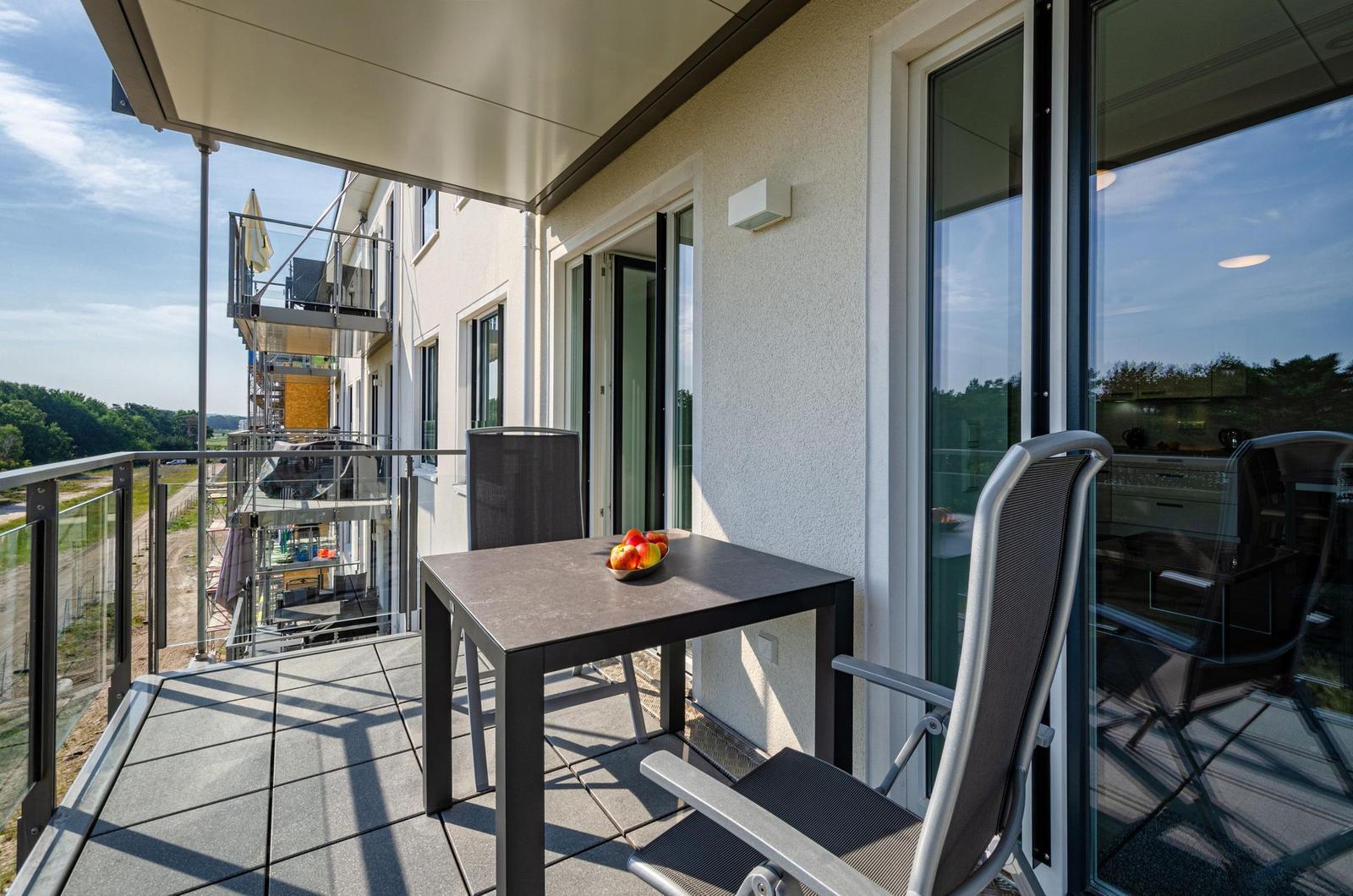 Terrasse mit Tisch, Stühlen und Obst. Blick auf Gebäude und Wald.