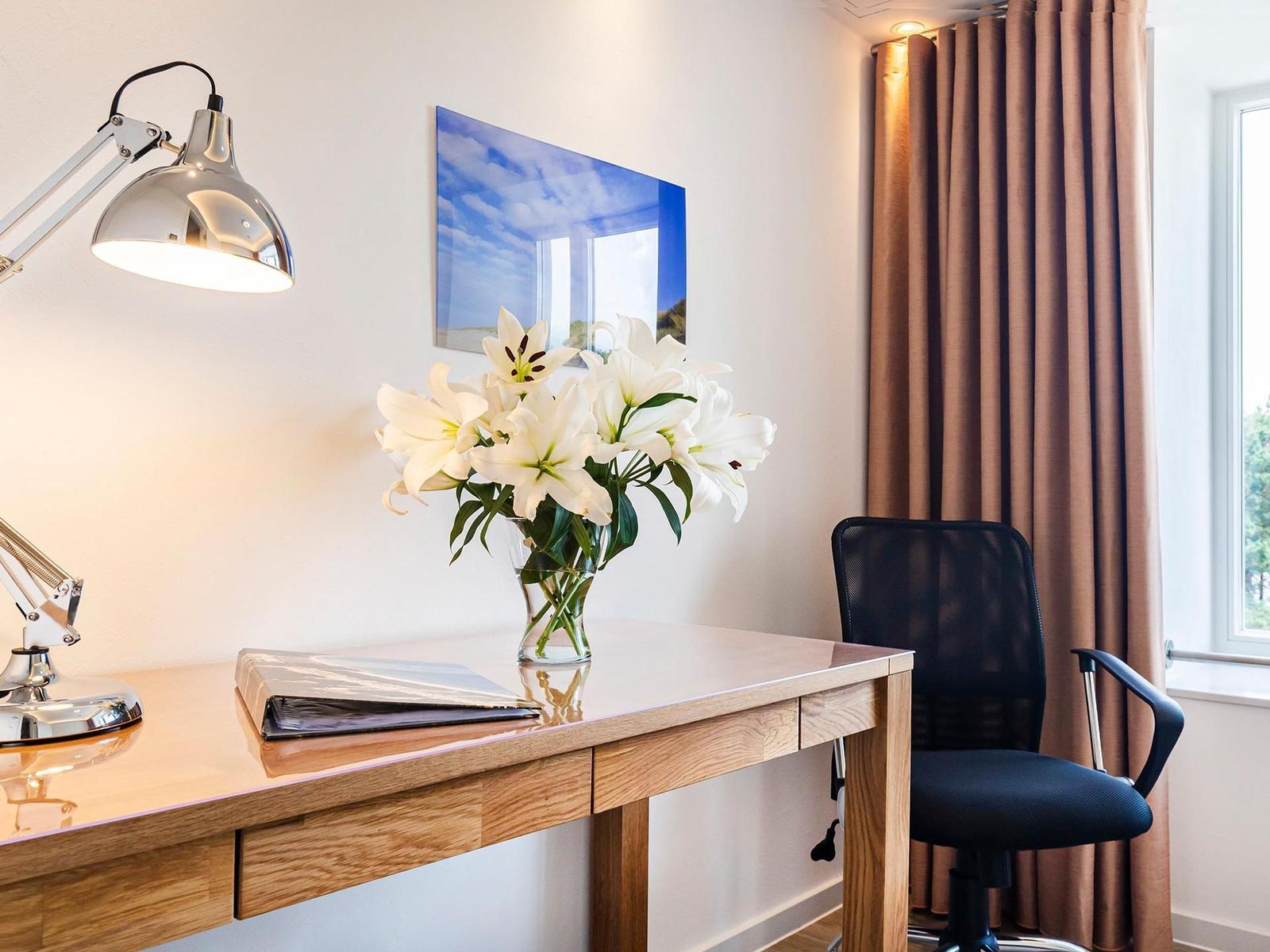 Schreibtisch mit Stuhl, Blumen und Lampe vor Fenster mit Vorhängen