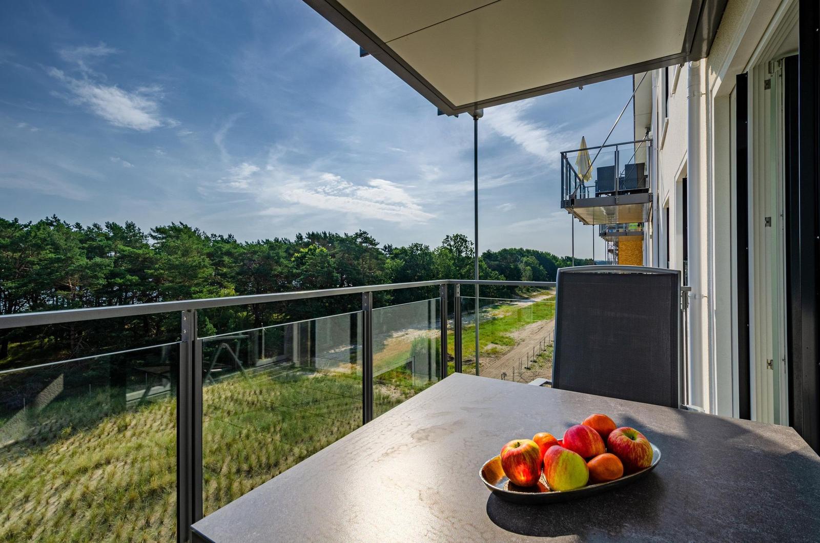Terrasse mit Tisch, Obst und Blick auf Wald und Himmel.