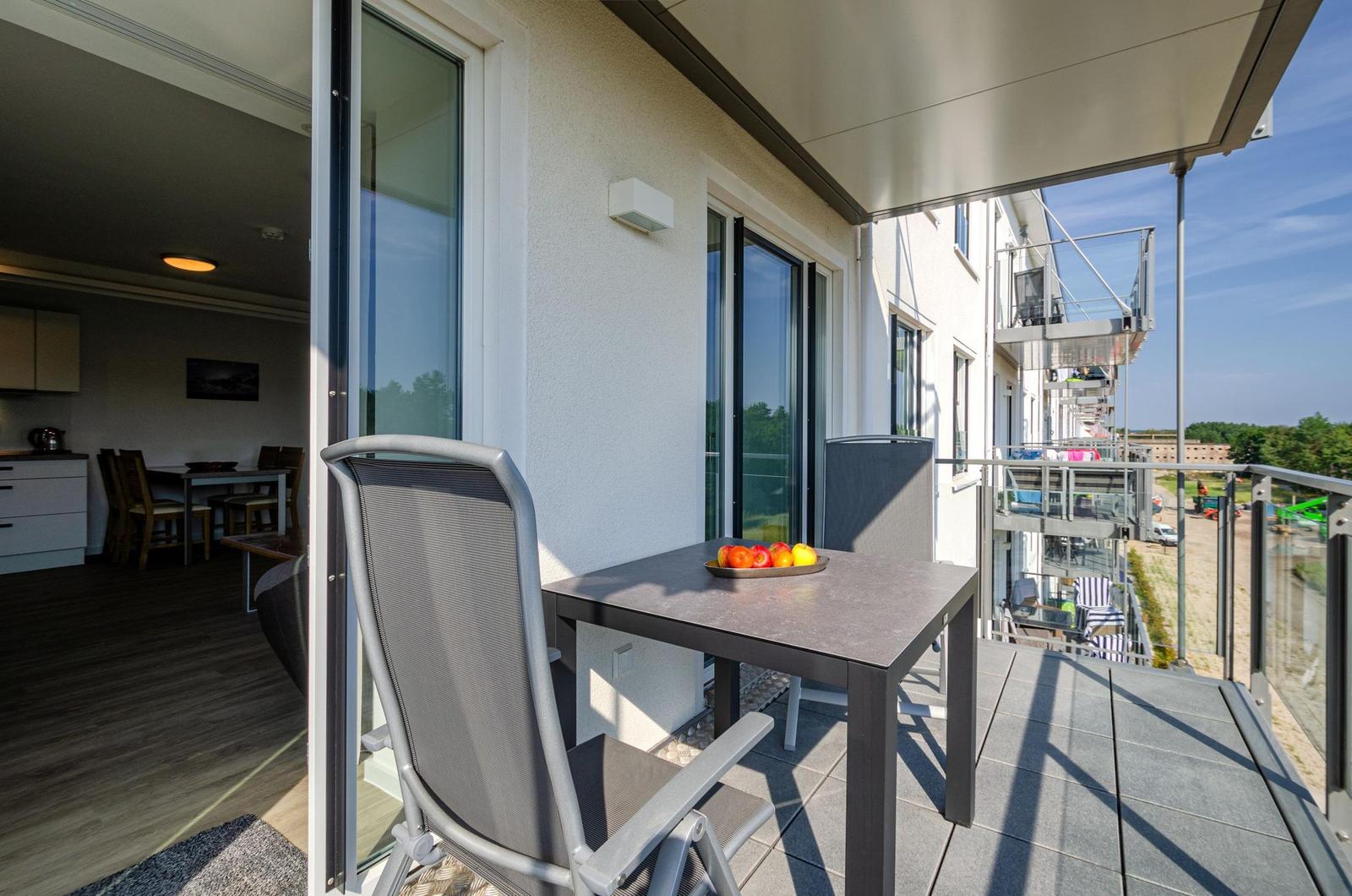Terrasse mit Tisch, Stühlen und Obstschale. Blick auf Wohnhaus und Landschaft.
