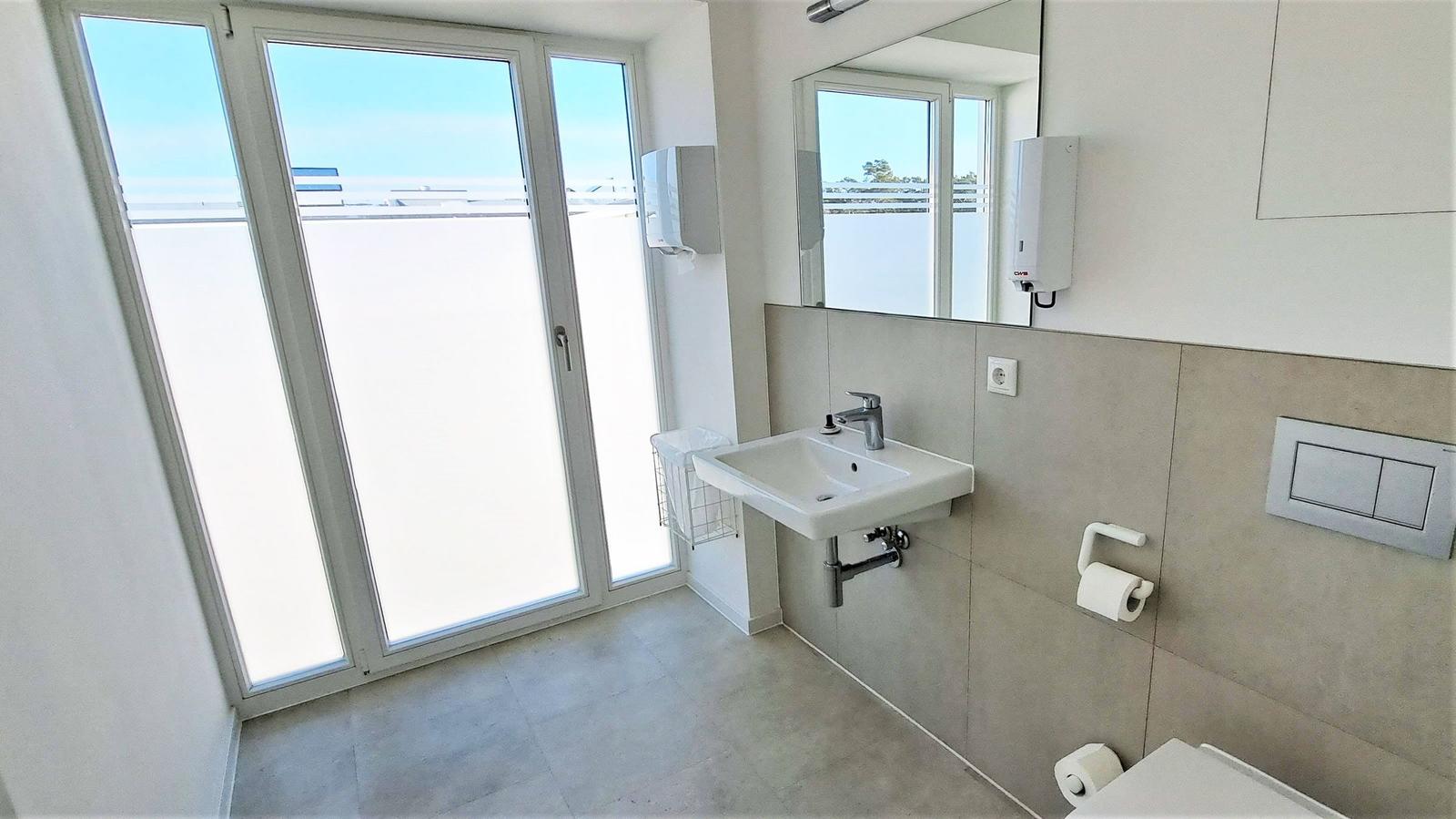 Badezimmer mit Waschbecken, Spiegel und Glastür zum Balkon.
