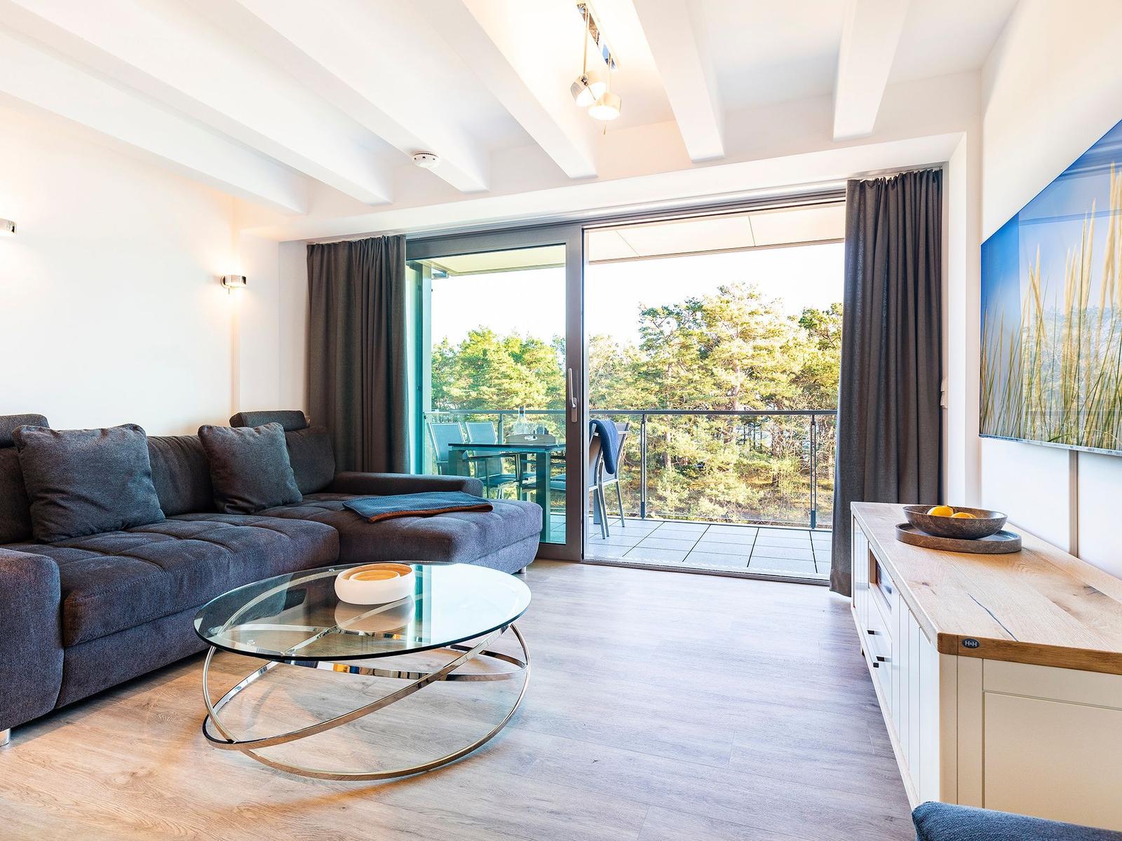 Wohnzimmer mit Sofa, Glas-Tisch und Balkonblick durch Glastüren.