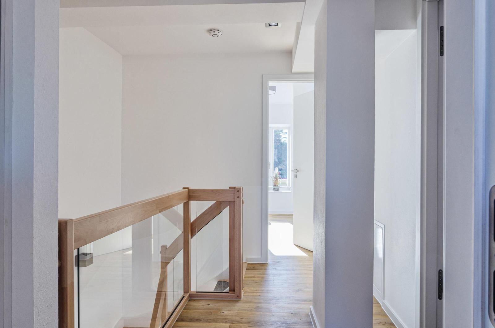 Hausflur mit Holz- und Glasgeländer, Holzboden und weiß getünchten Wänden.