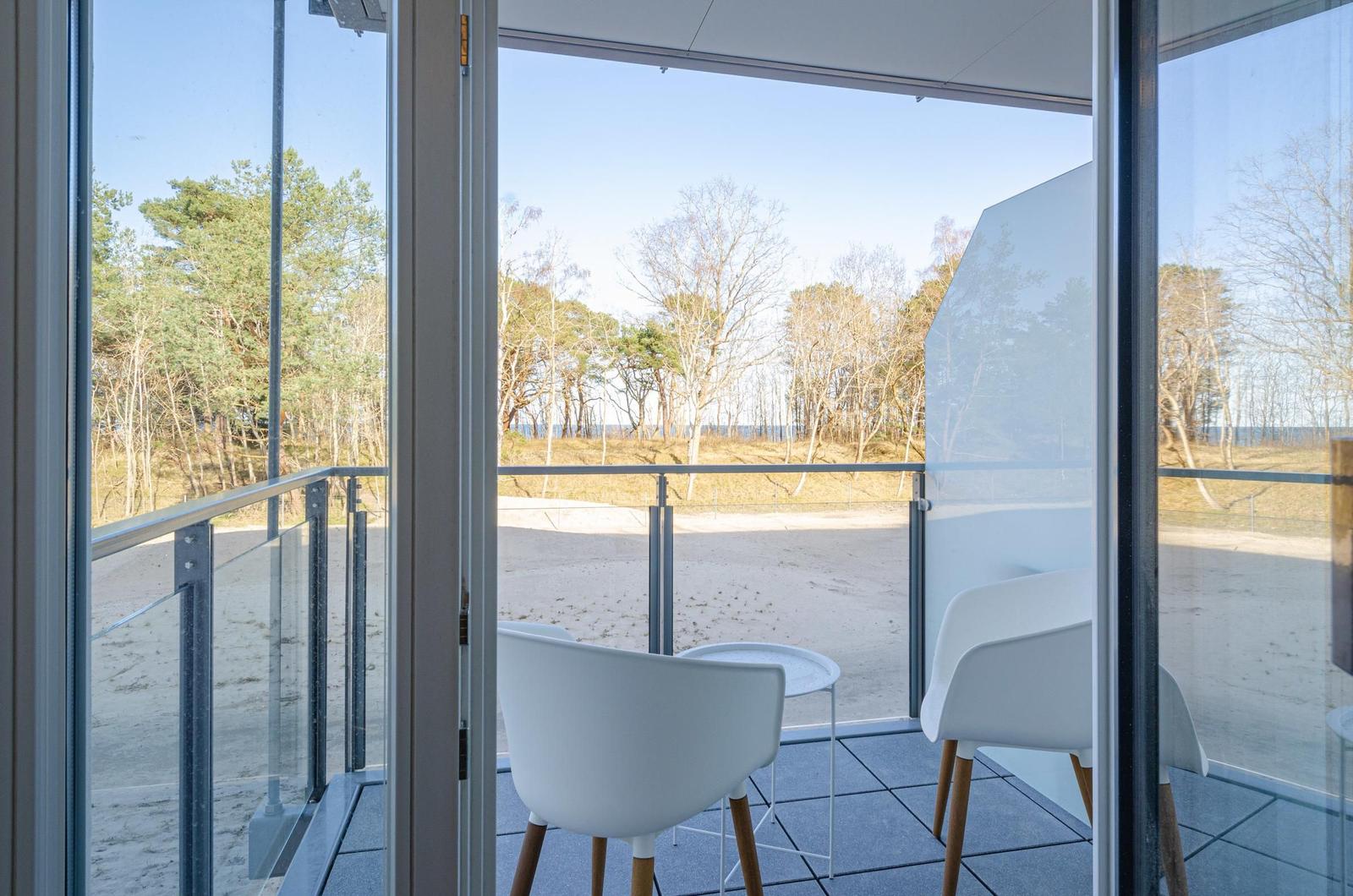 Terrasse mit weißen Stühlen und Tisch. Blick auf Wald und Strand.