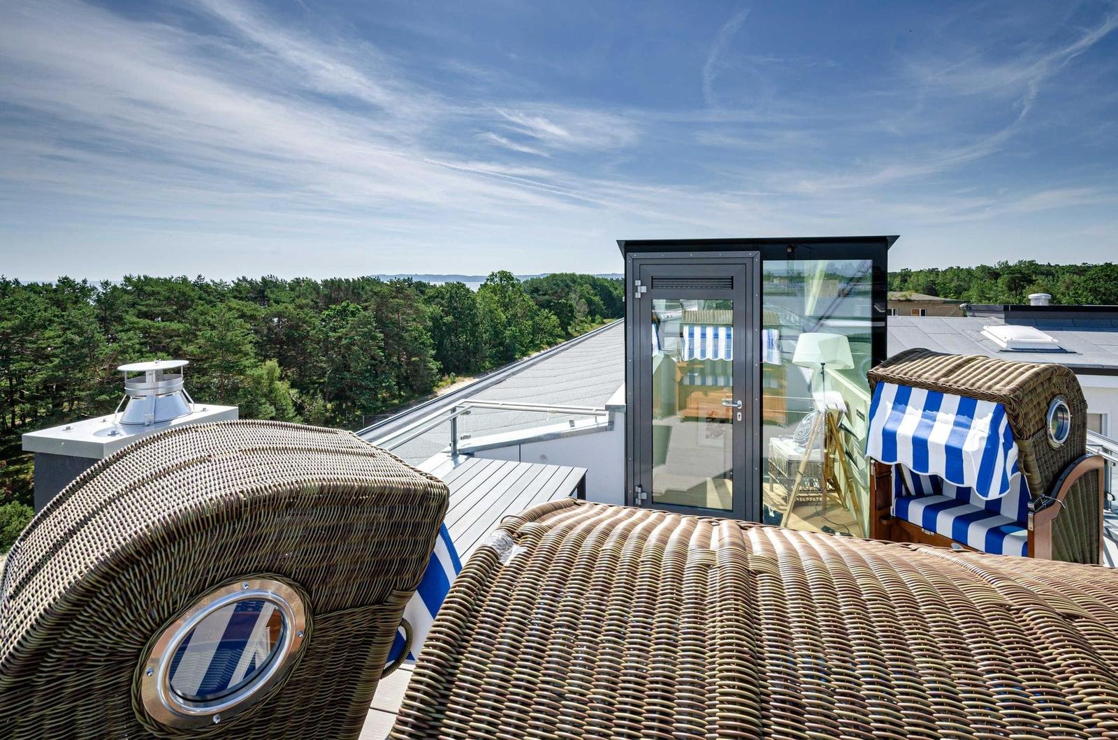 Terrasse mit Rattanliegen und Blick auf Wald und Himmel.