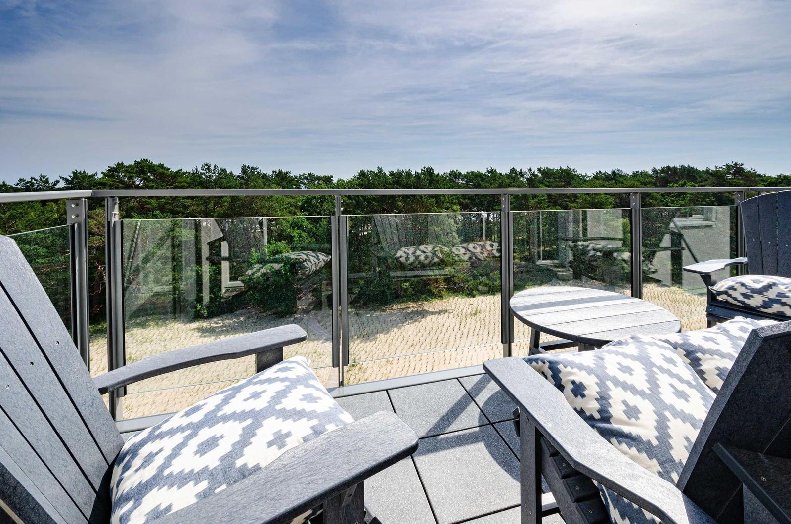Terrasse mit Sitzgelegenheiten und Blick auf Wald und Sandstrand.