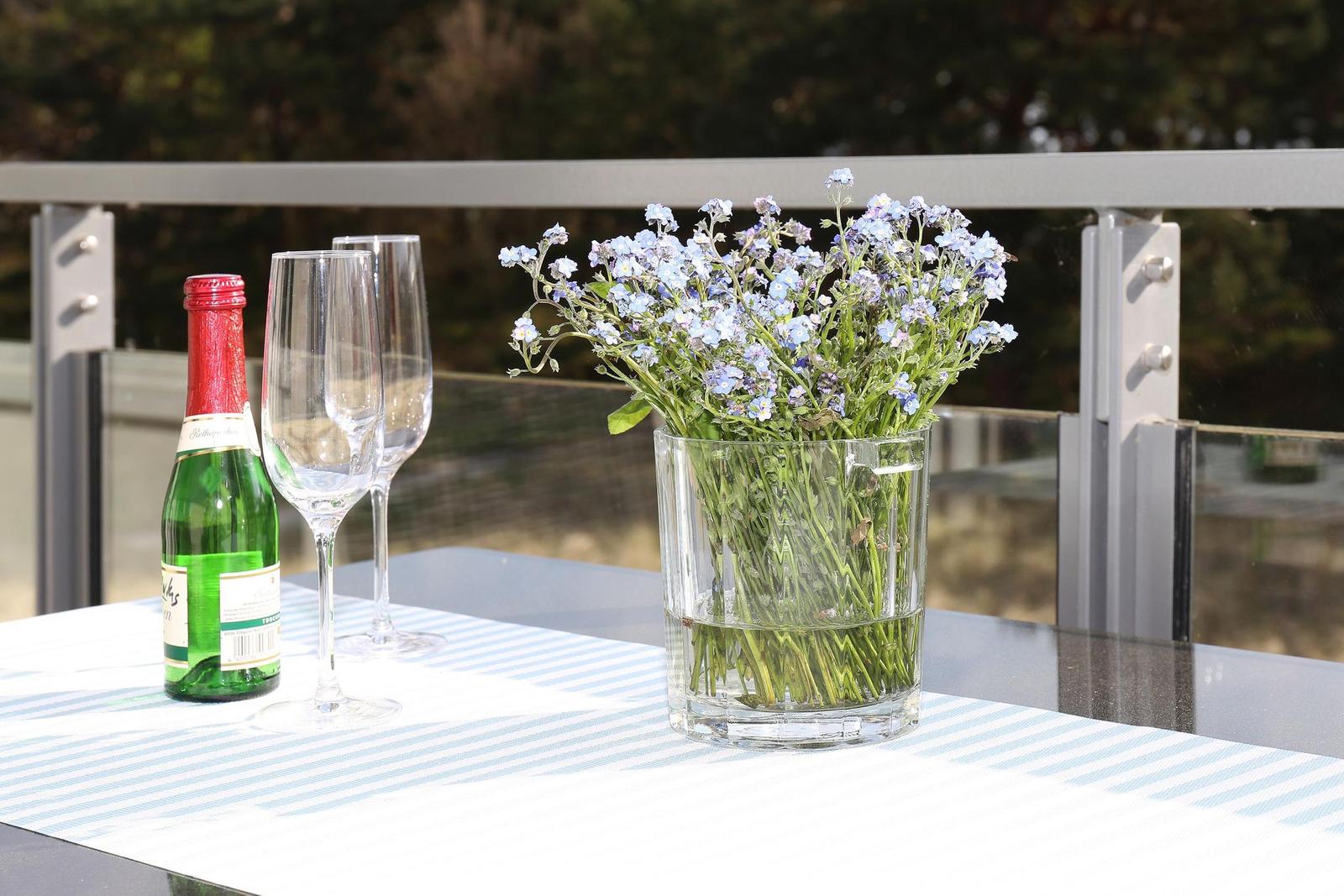 Auf der Terrasse steht ein Tisch mit Blumen, Wein und Gläsern.