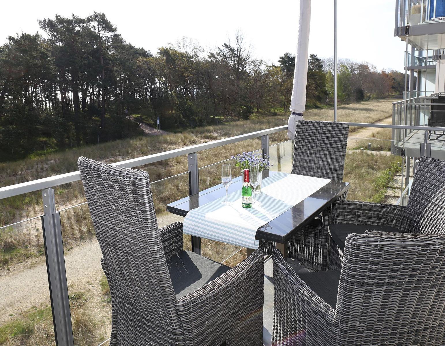 Terrasse mit Tisch und Stühlen, Blick auf Wald und Strand.