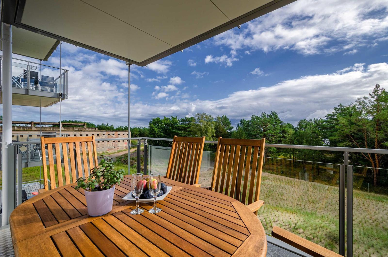 Terrasse mit Holztisch, Stühlen und Blick auf Wald und Himmel.