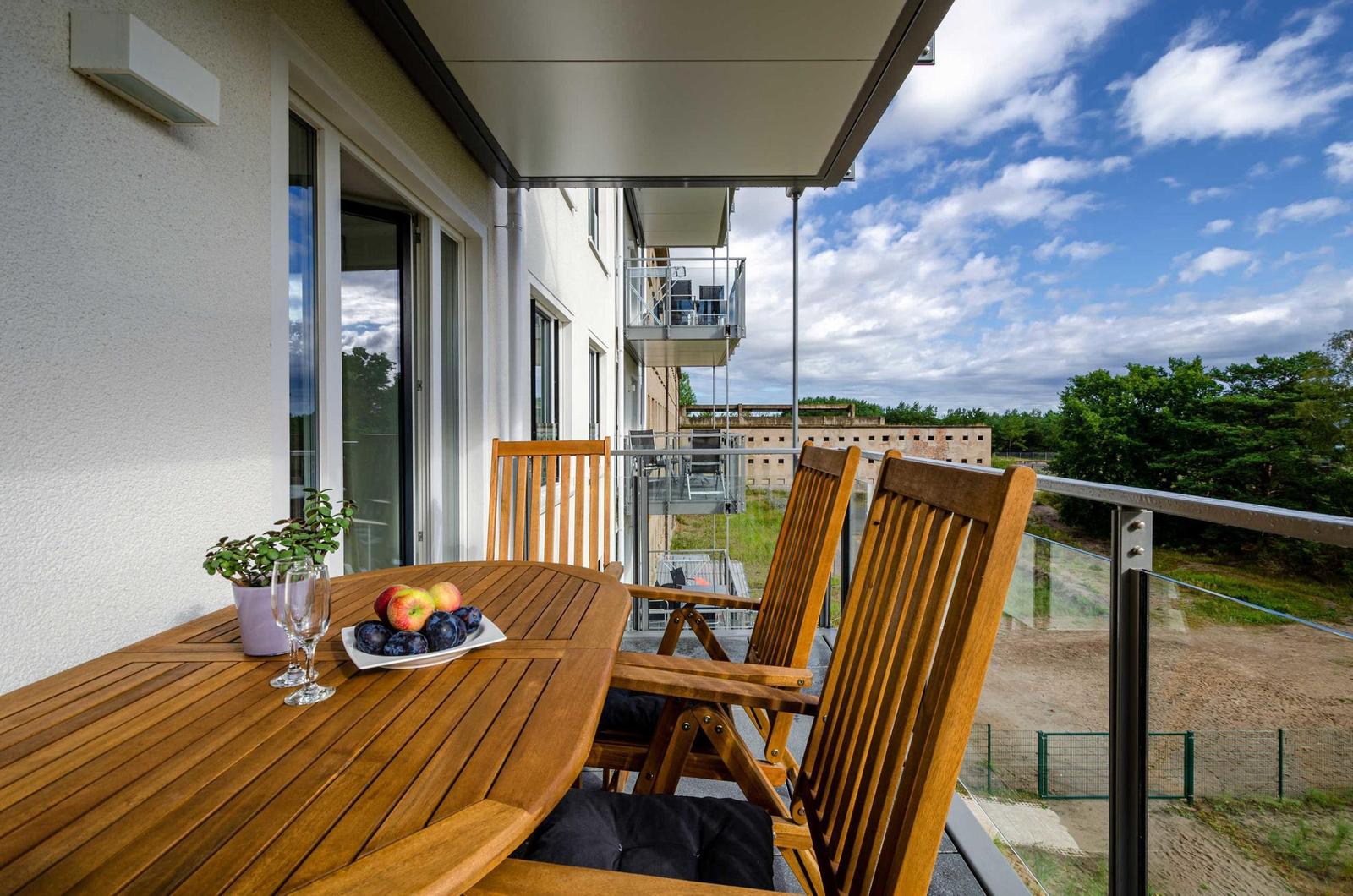 Terrasse mit Holztisch, Stühlen, Obst und Pflanze. Blick auf Gebäude und Bäume.
