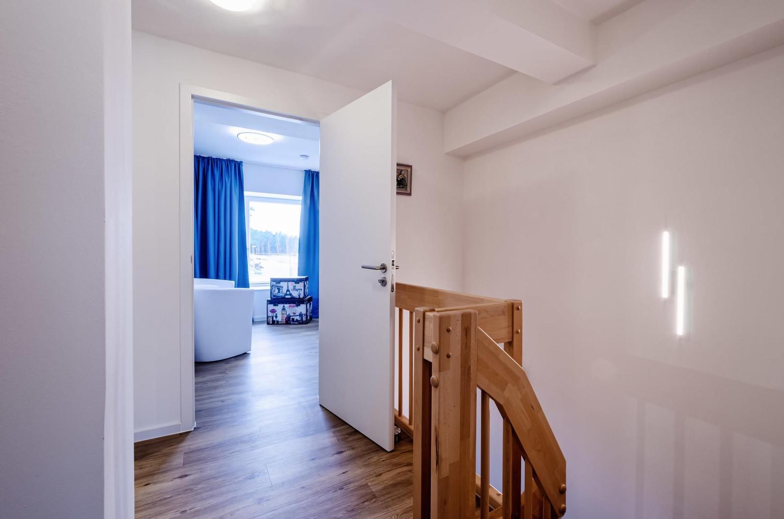Haus mit Holzgeländer, Tür und Blick in Wohnzimmer mit blauen Vorhängen.