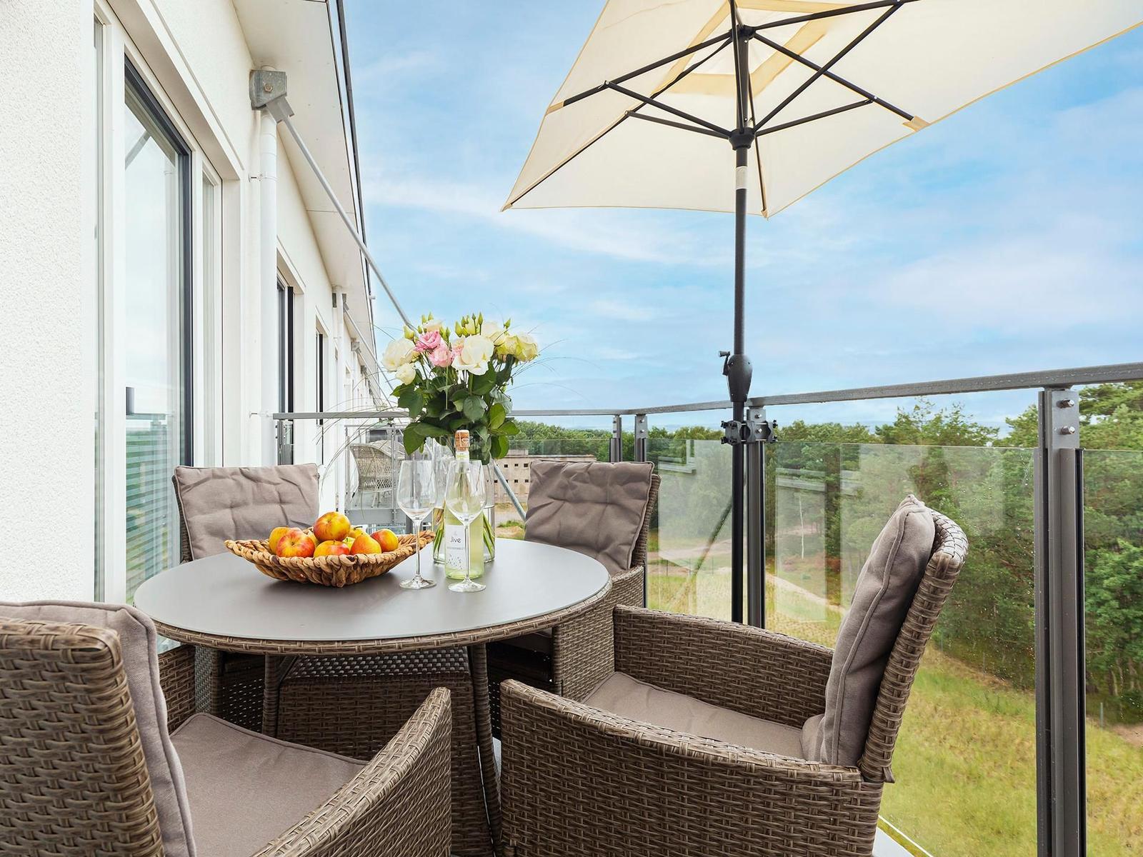 Terrasse mit Tisch, Stühlen und Sonnenschirm. Blumen und Obst auf dem Tisch.
