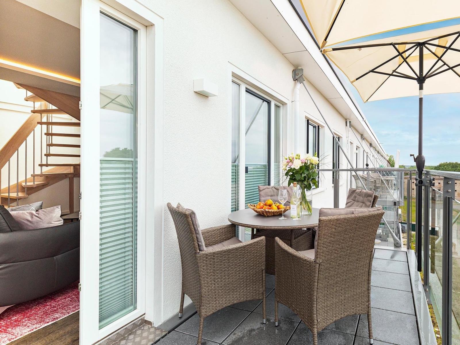 Terrasse mit Tisch, Stühlen und Sonnenschutz. Blick auf Wohnbereich mit Sofa und Treppe.