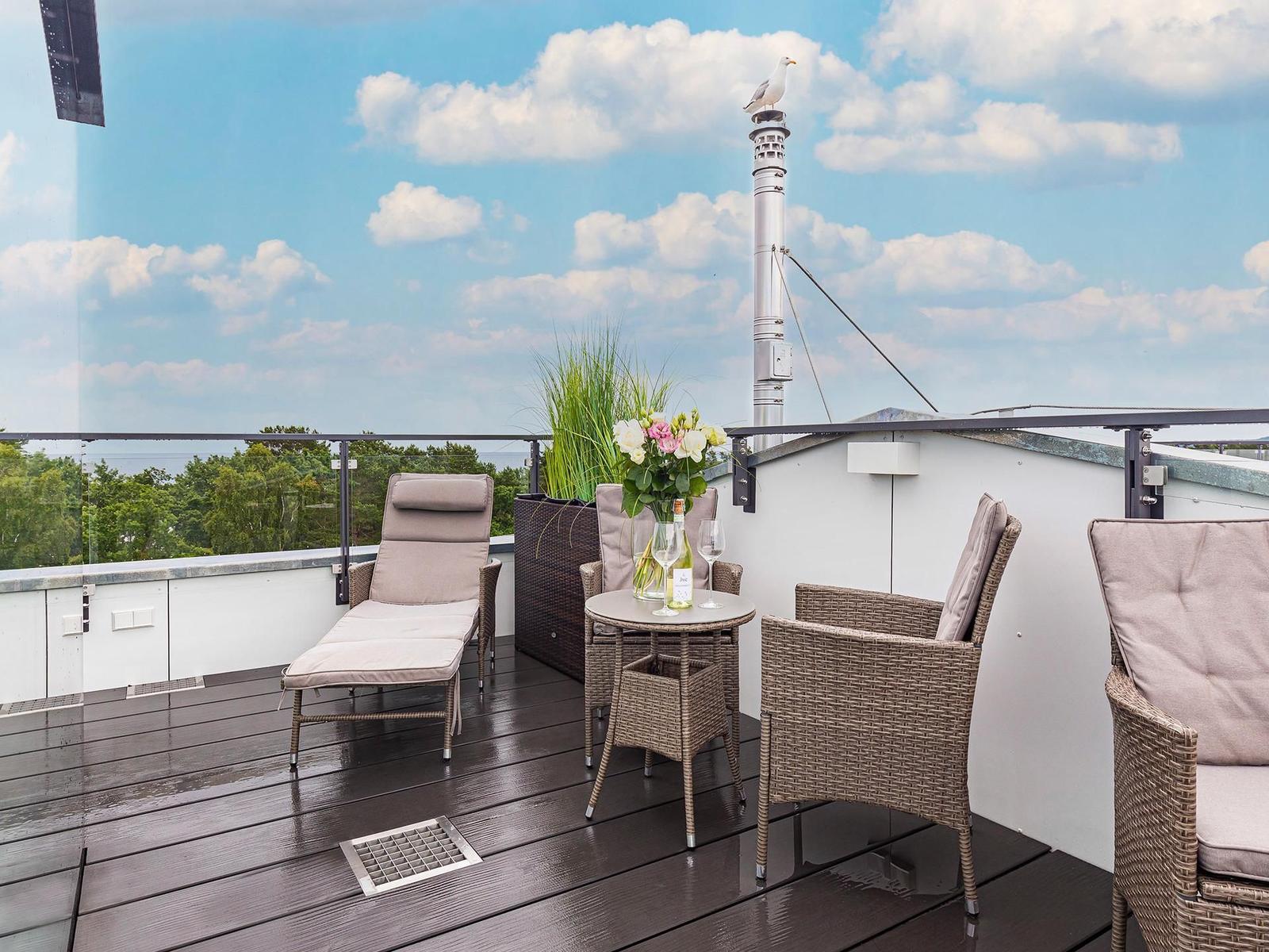 Dachterrasse mit Sitzgelegenheiten und Blick auf Himmel und Bäume.
