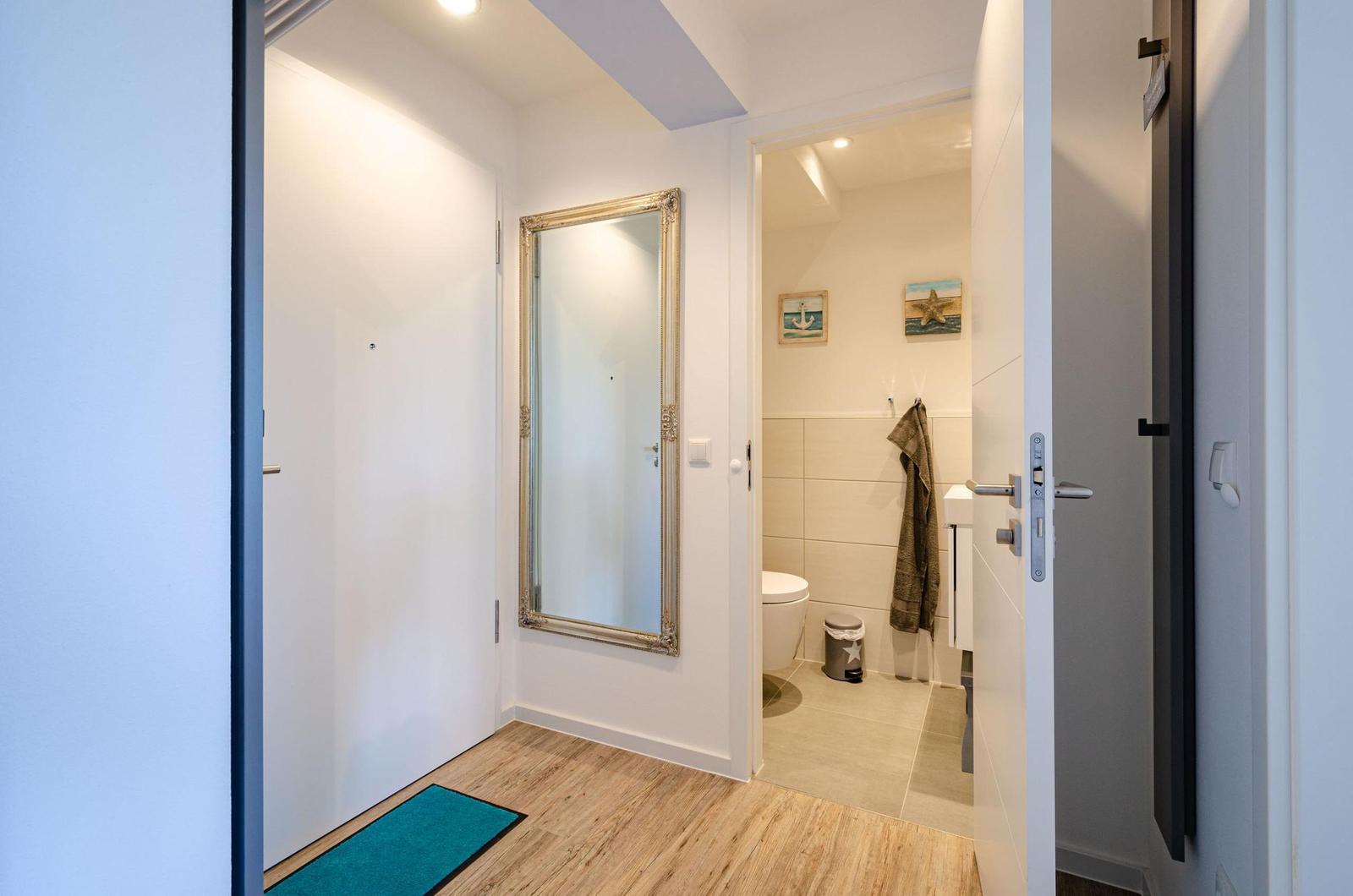 Hallway with mirror and door to bathroom. Bathroom with toilet and towel.