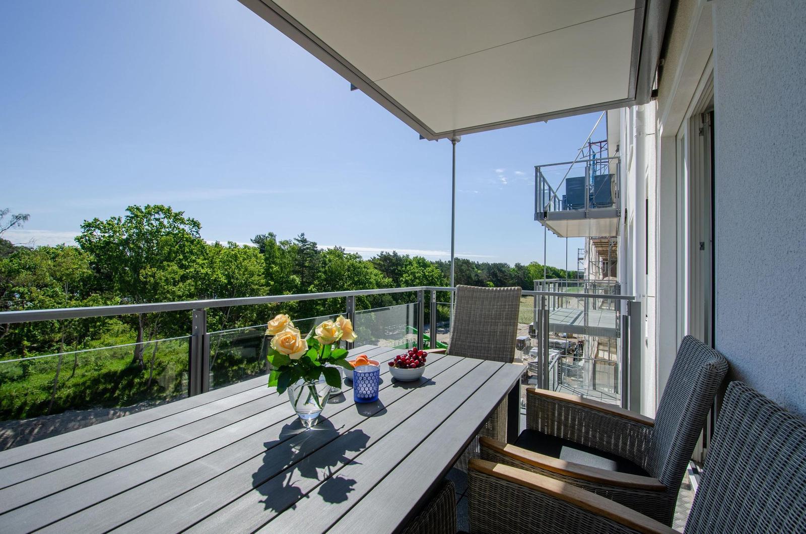 Terrace with table, chairs, and view of green trees under clear sky.