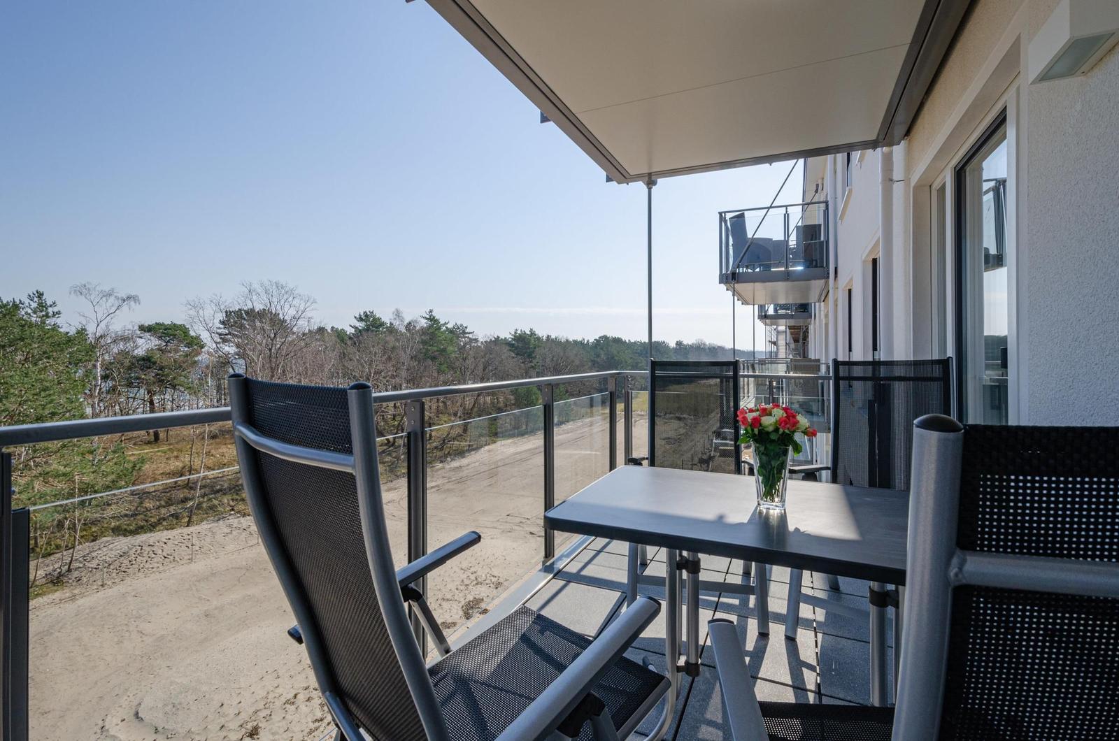 Balcony with table and chairs, view of forest and beach.