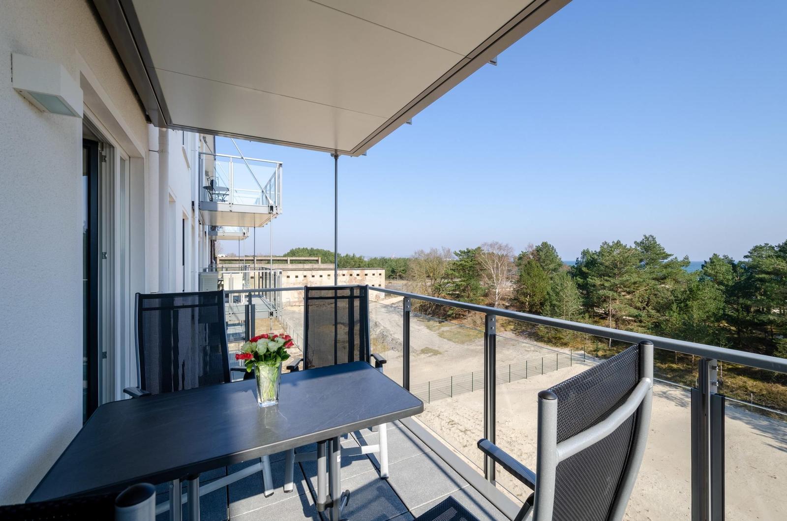 Terrace with table and chairs, view of forest and beach.