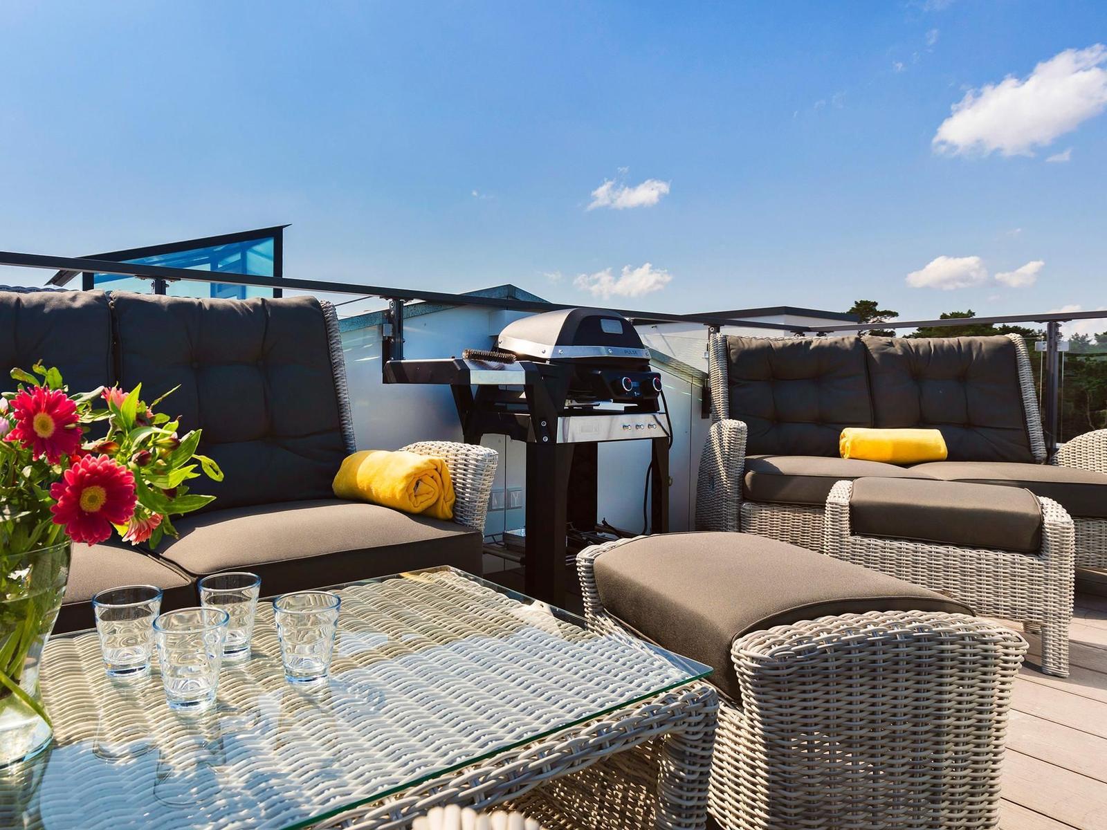 Terrasse mit Sitzgruppe, Grill und Tisch mit Gläsern und Blumen.