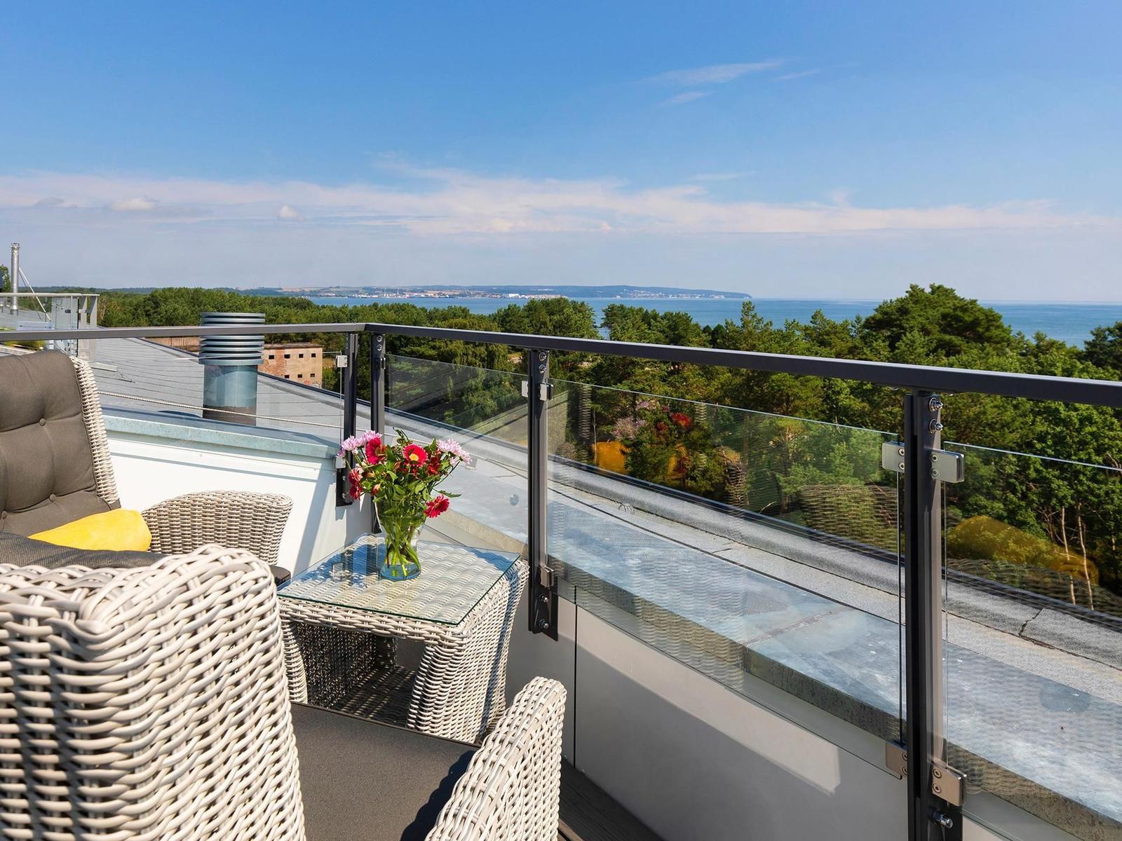 Terrasse mit Sitzgruppe und Blick auf Meer und Wald.