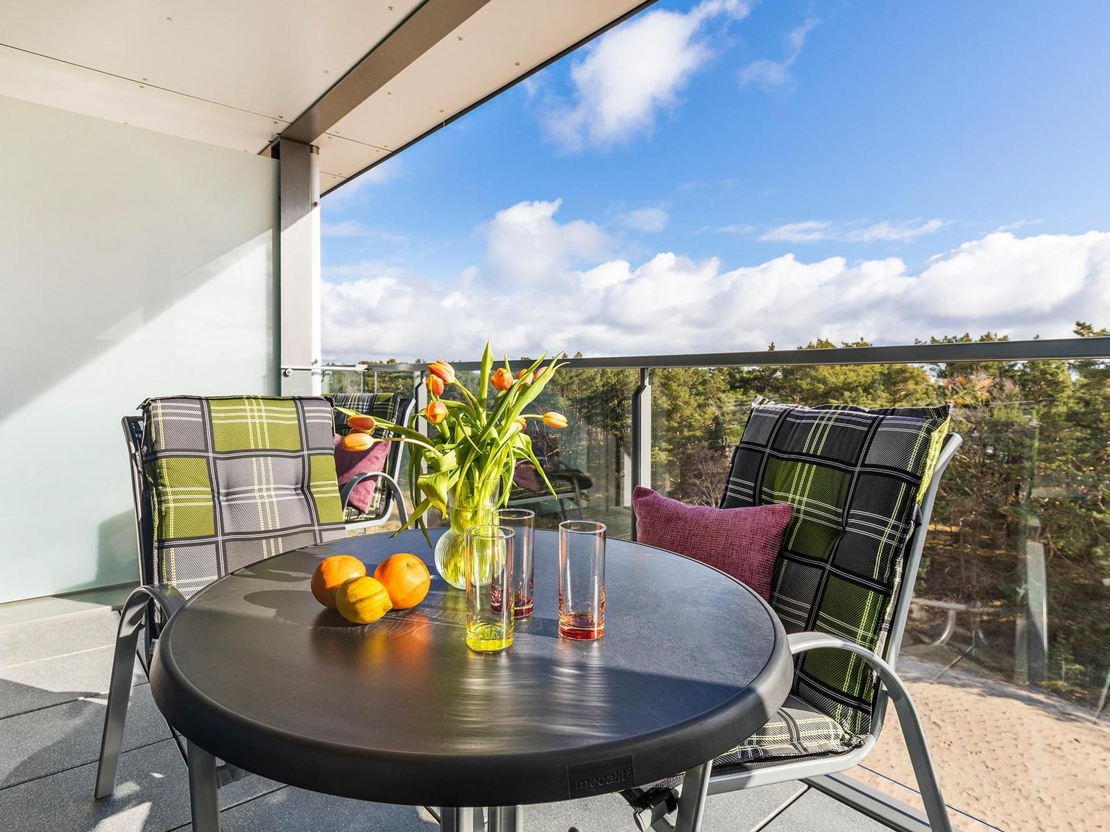 Terrasse mit Tisch, Stühlen und Blumen. Blick auf Wald und Himmel.