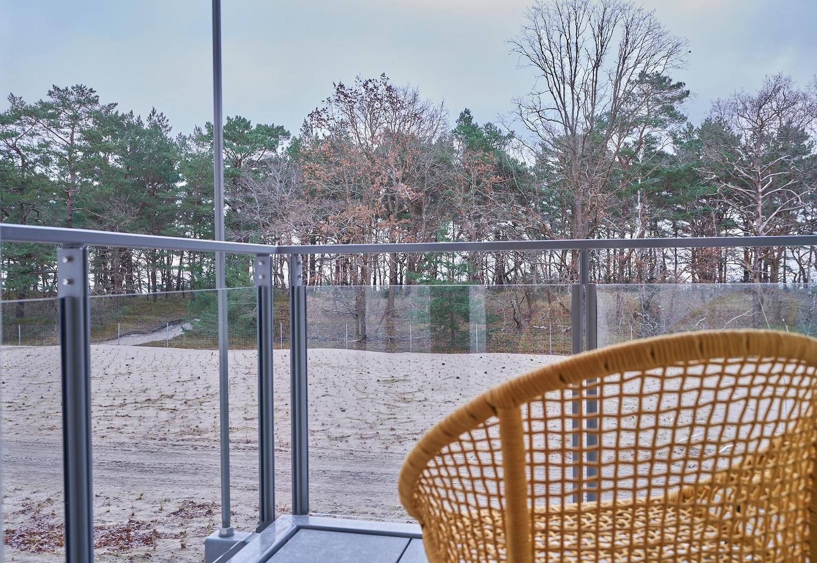 Terrasse mit Stuhl und Blick auf Wald und Strand.