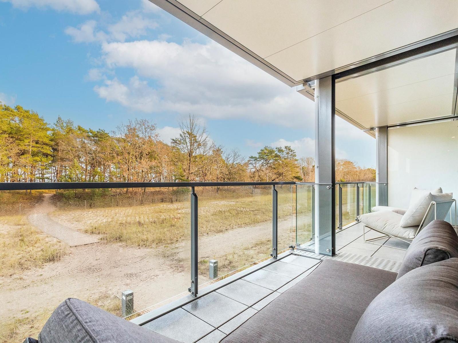Terrasse mit Glasgeländer und Sitzmöbeln. Blick auf Wald und Himmel.