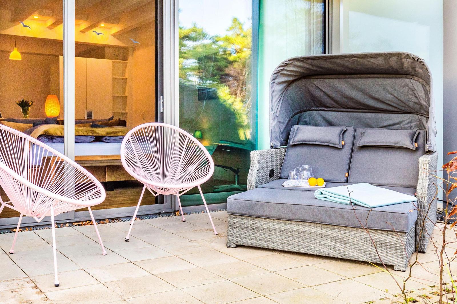 Terrasse mit Liegesofa, zwei Stühlen und Blick in das Schlafzimmer.