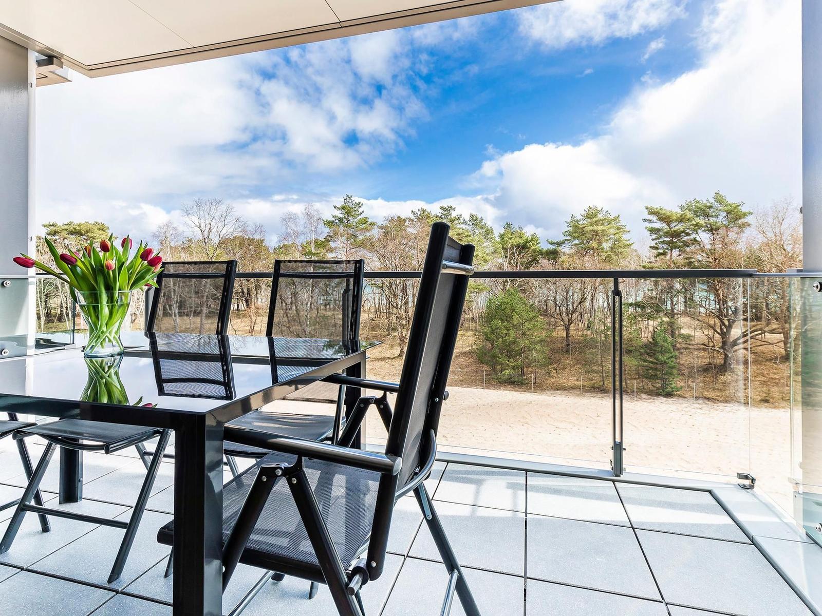 Terrasse mit Tisch, Stühlen und Tulpenblumen. Blick auf Wald und Himmel.