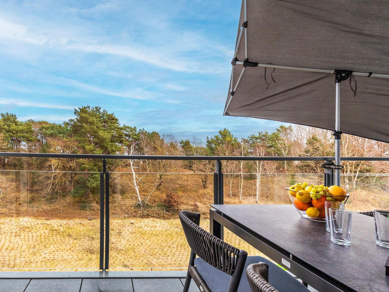 Terrasse mit Tisch, Stühlen und Sonnenschutz. Blick auf Wald und Himmel.