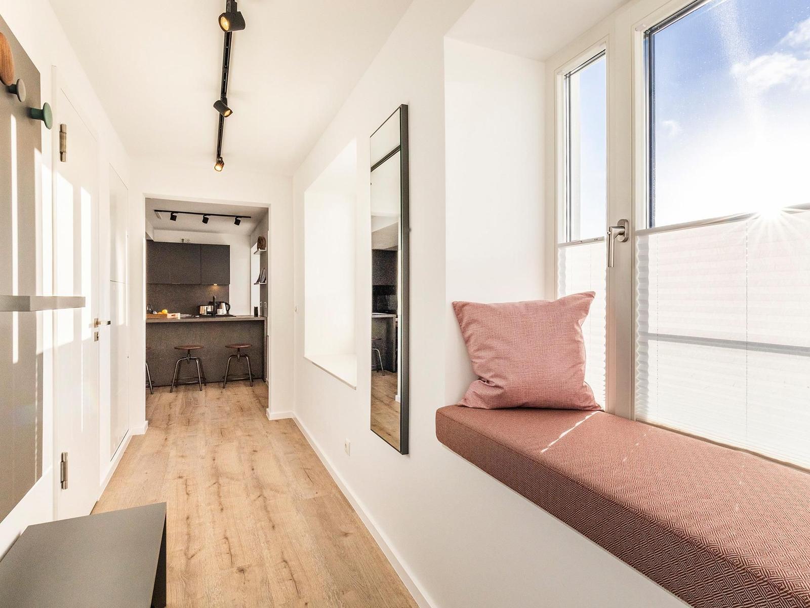 Ein Fensterbank mit Kissen, Blick in Küche mit Holzboden und Spiegelfläche an der Wand.