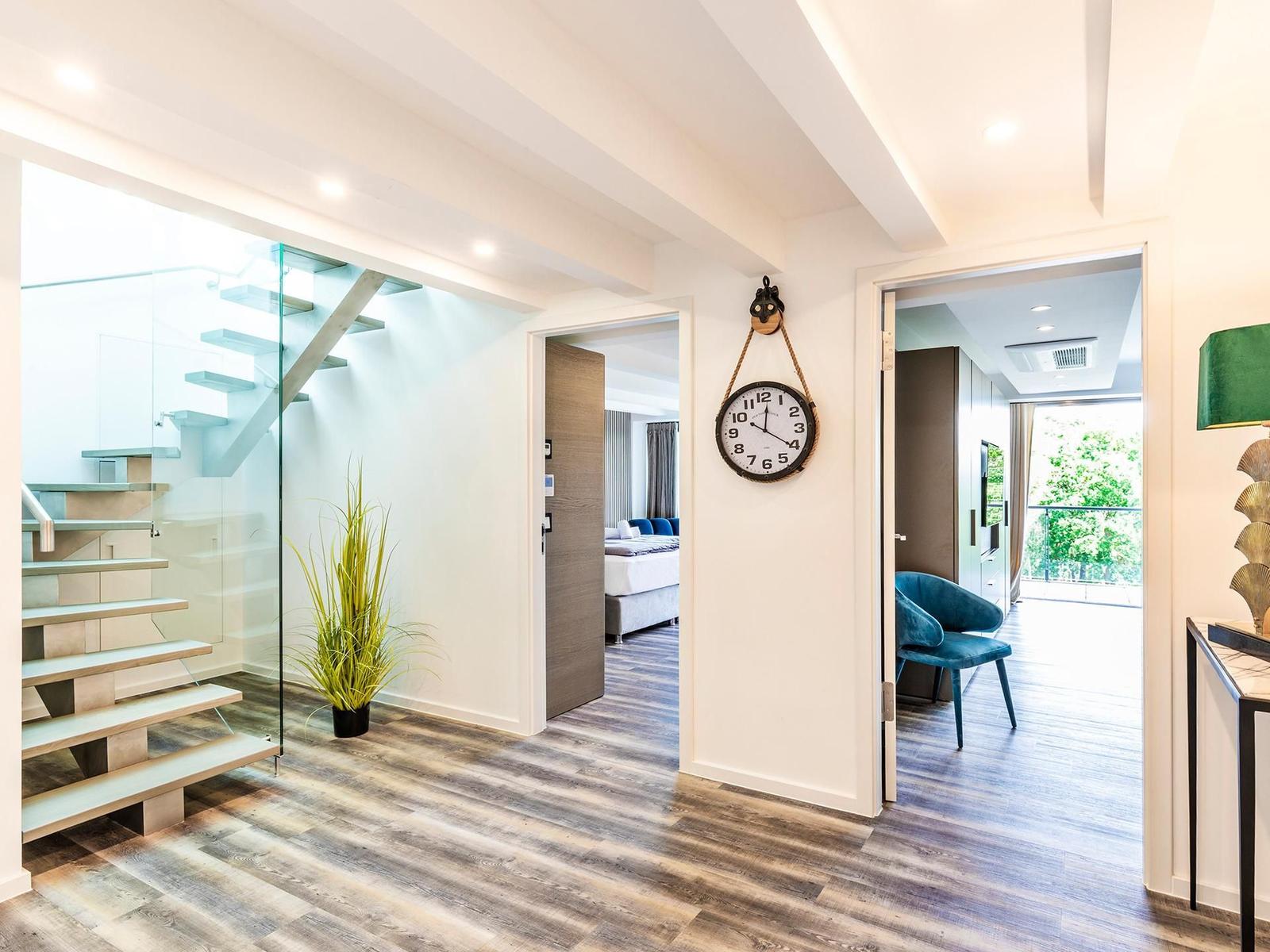 Haus mit Glasgeländer-Treppe, Wanduhr und Blick in Schlaf- und Wohnbereich.