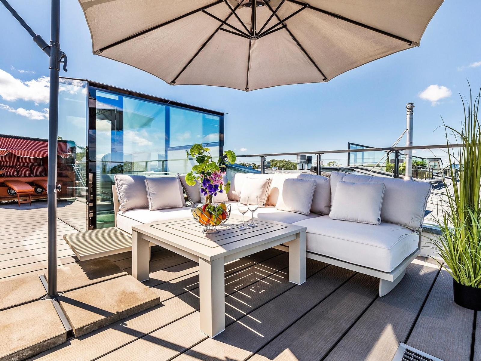 Terrasse mit Sitzgruppe, Sonnenschutz und Tisch mit Obst und Blumen.