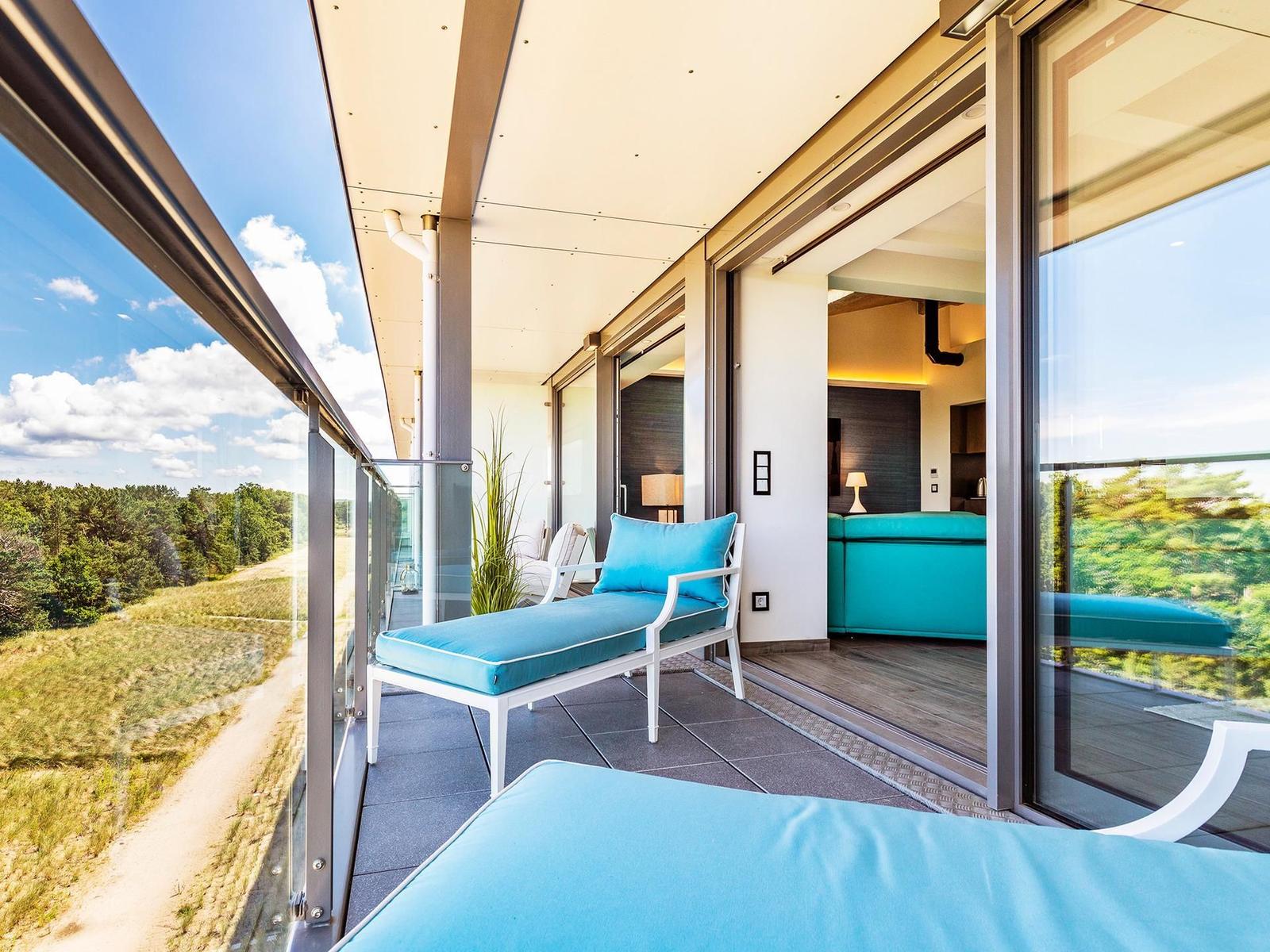 Terrasse mit blauen Liegen und Blick auf Wald und Himmel.
