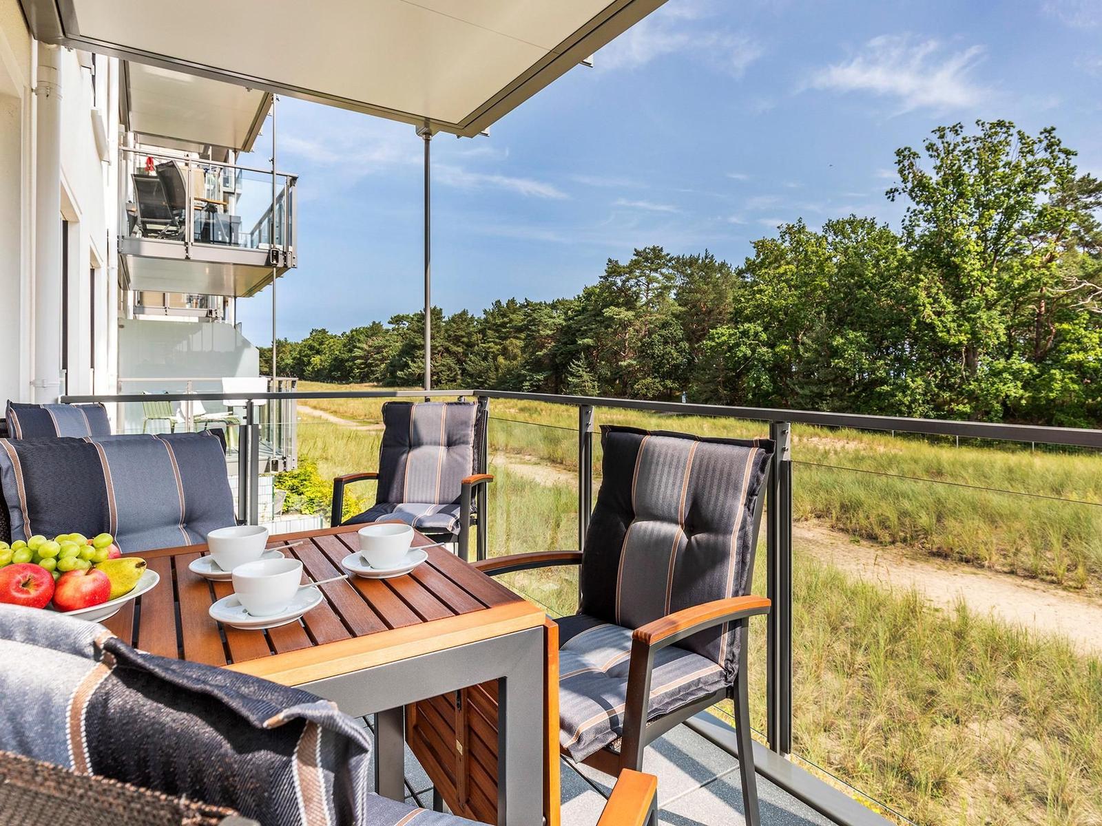 Terrace with table, chairs, and view of forest. Sunshade and fruit on table.