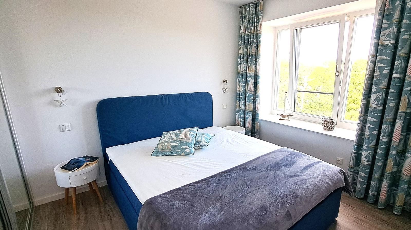Bedroom with blue bed, window, and curtains with sailboat motif.