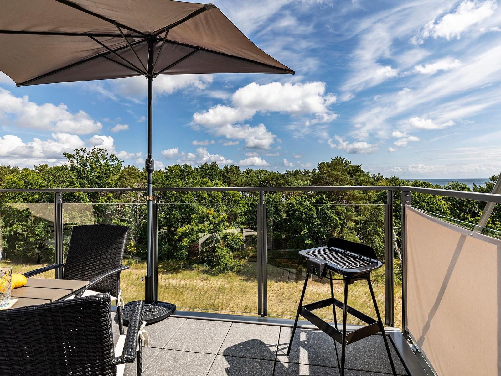 Terrace with umbrella, grill, and view of forest and sea.