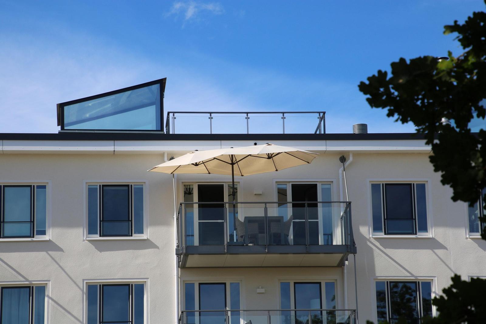 Fassade mit Balkon, Sonnenschirm und Glasgeländer unter blauem Himmel.