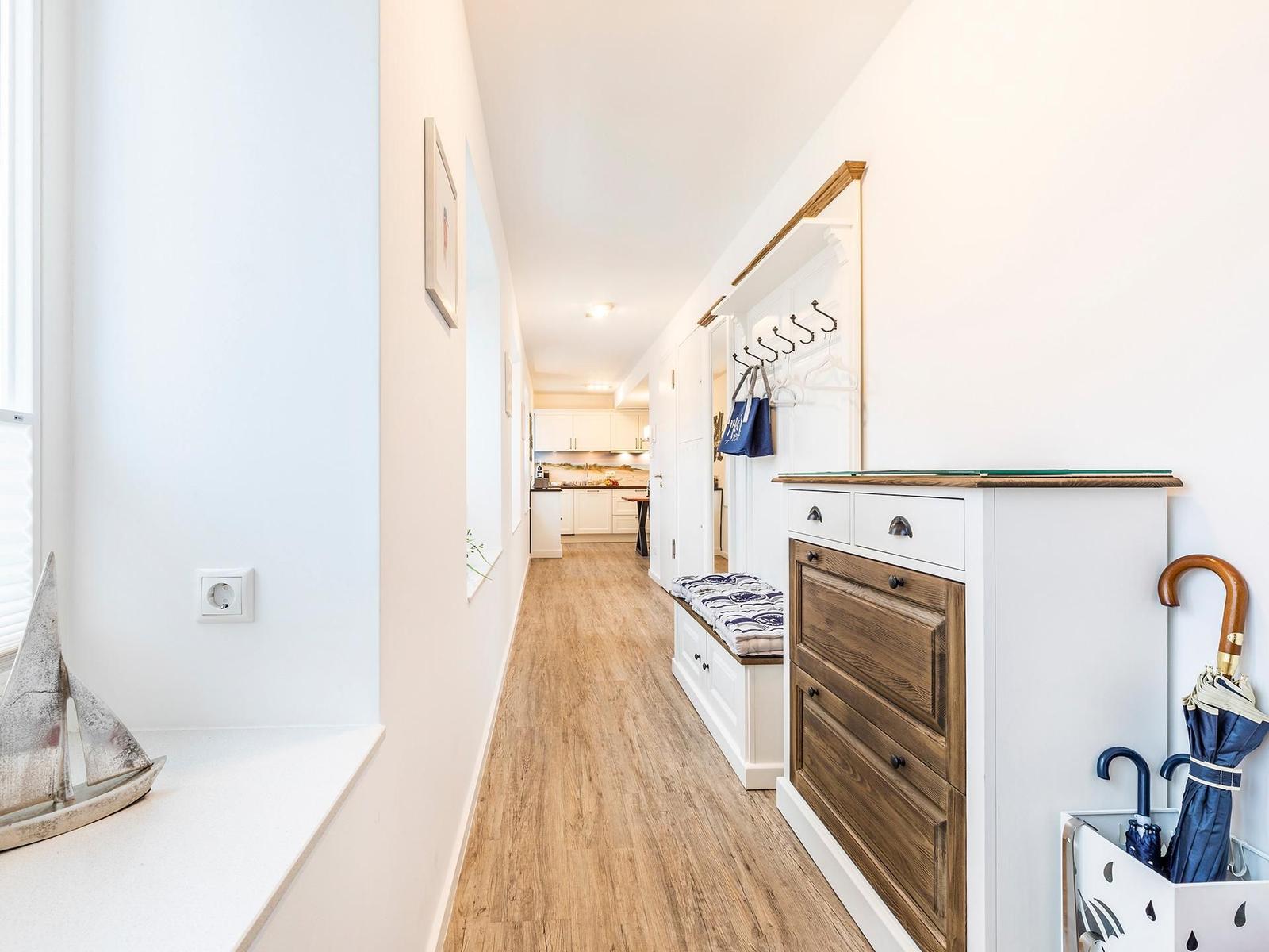 Flur mit Holzboden, Garderobe und Schuhschrank. Küchenbereich im Hintergrund.