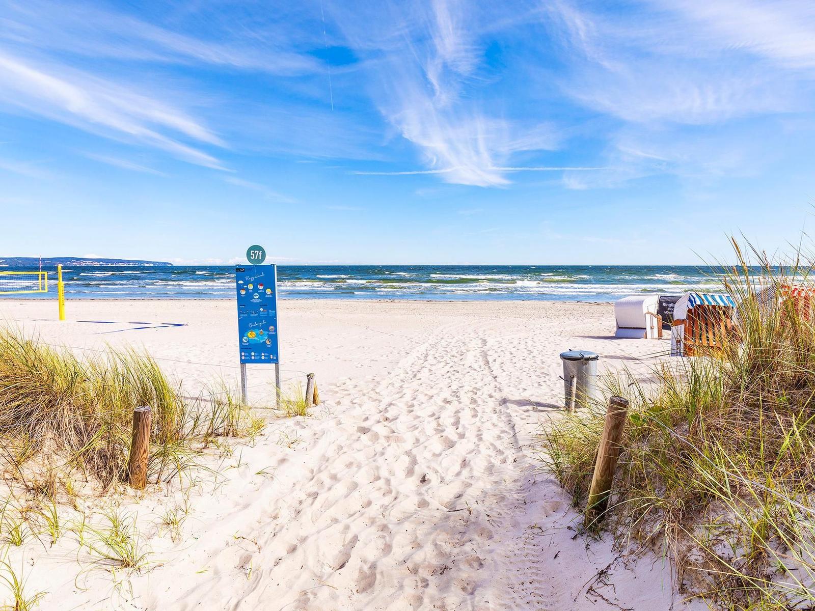 Sandweg führt zum Strand mit Strandkörben und Meer im Hintergrund.