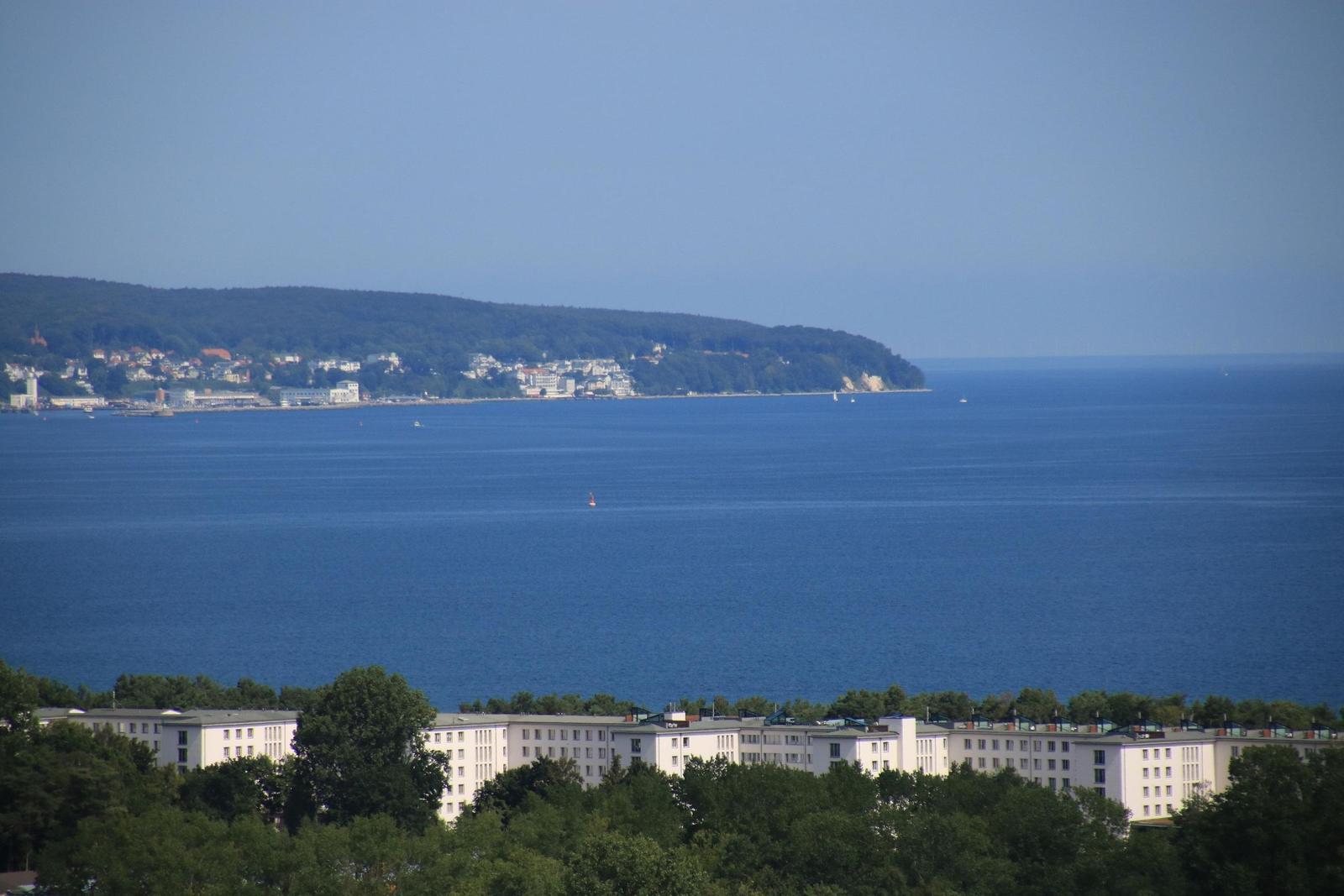 Blick auf das Meer und eine bewaldete Küstenlinie mit Gebäuden.