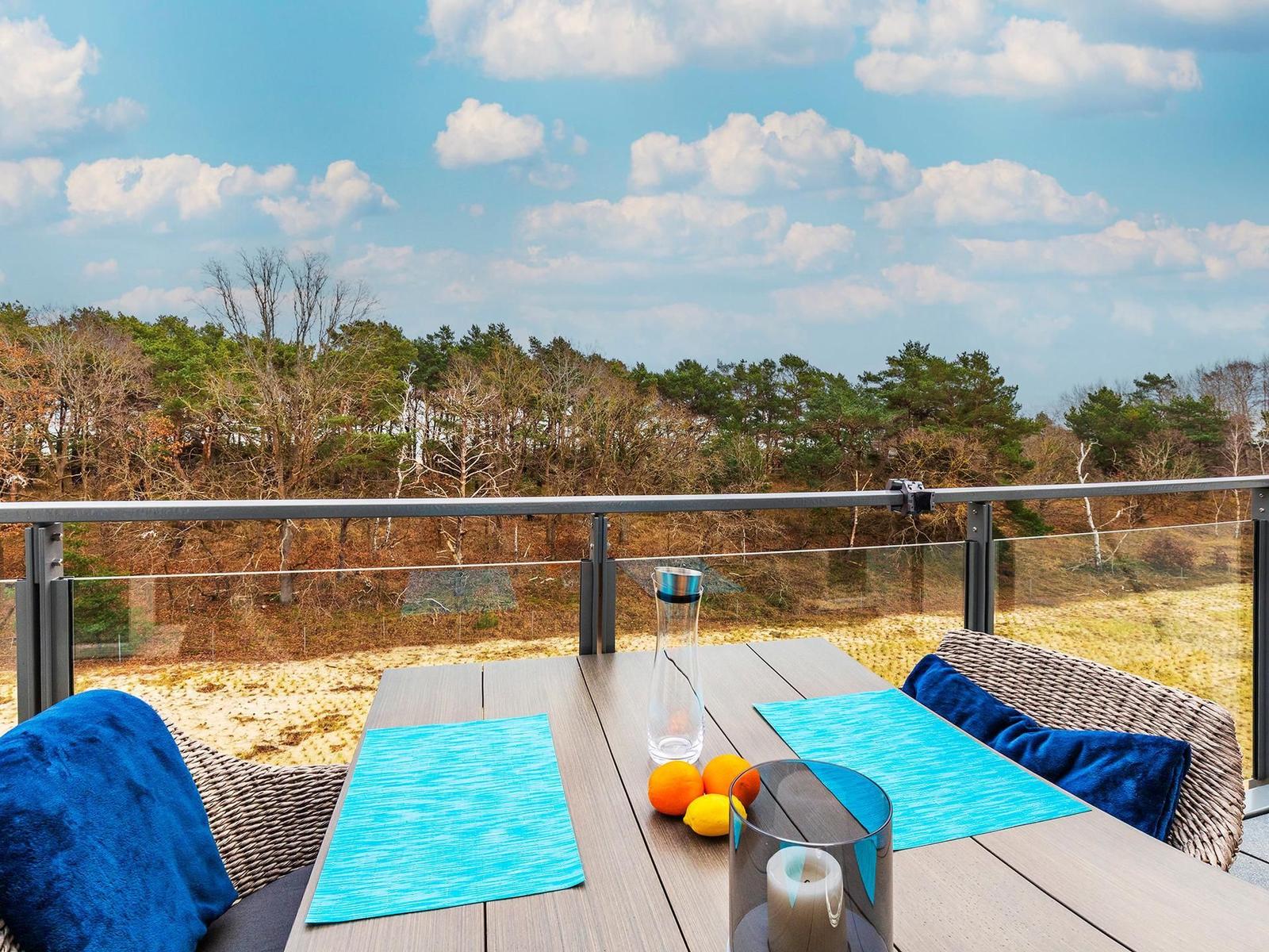 Terrasse mit Tisch, Stühlen und Blick auf Wald und Himmel.