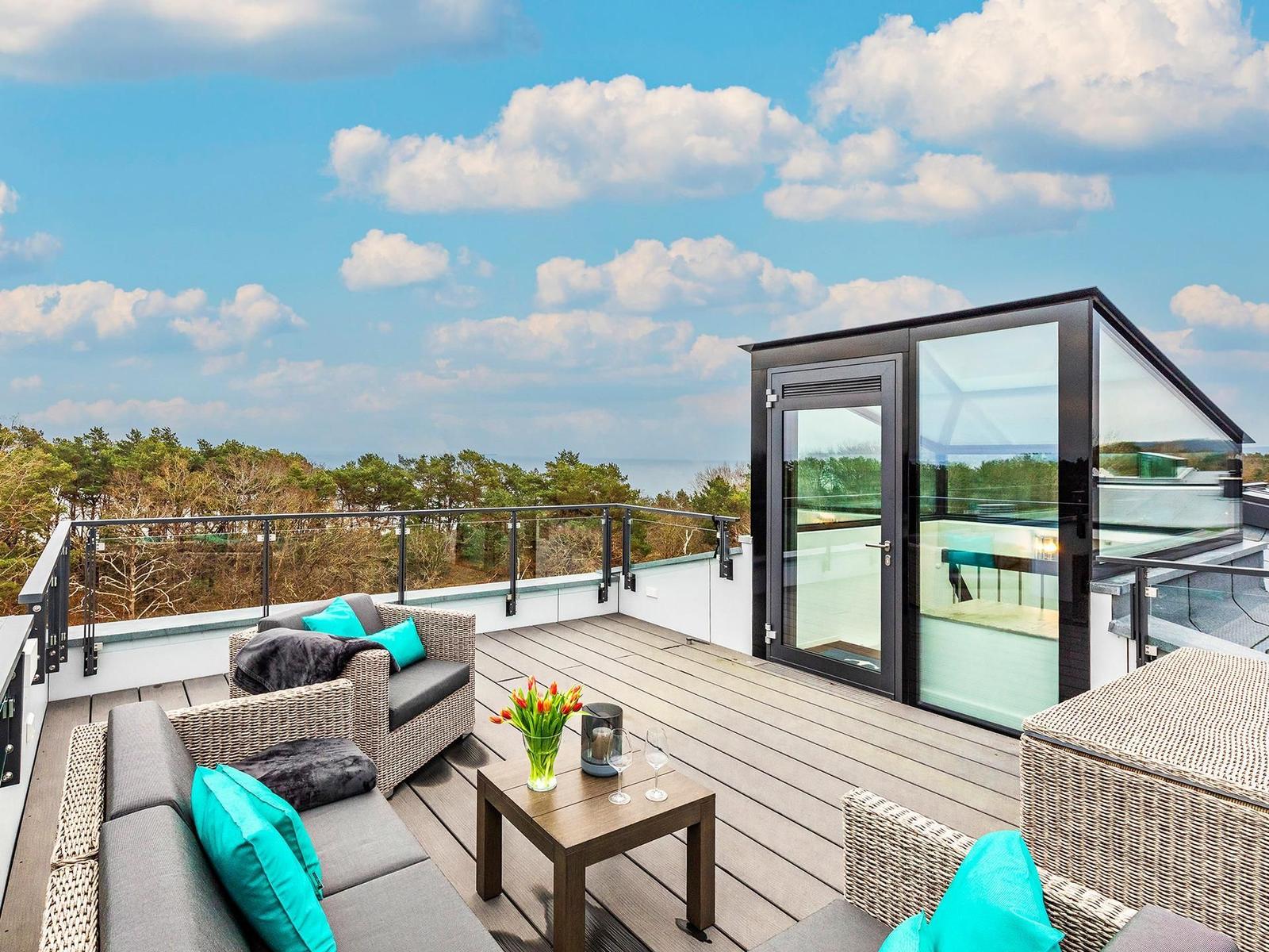 Terrasse mit Sitzgruppe und Blick auf Wald und Meer.