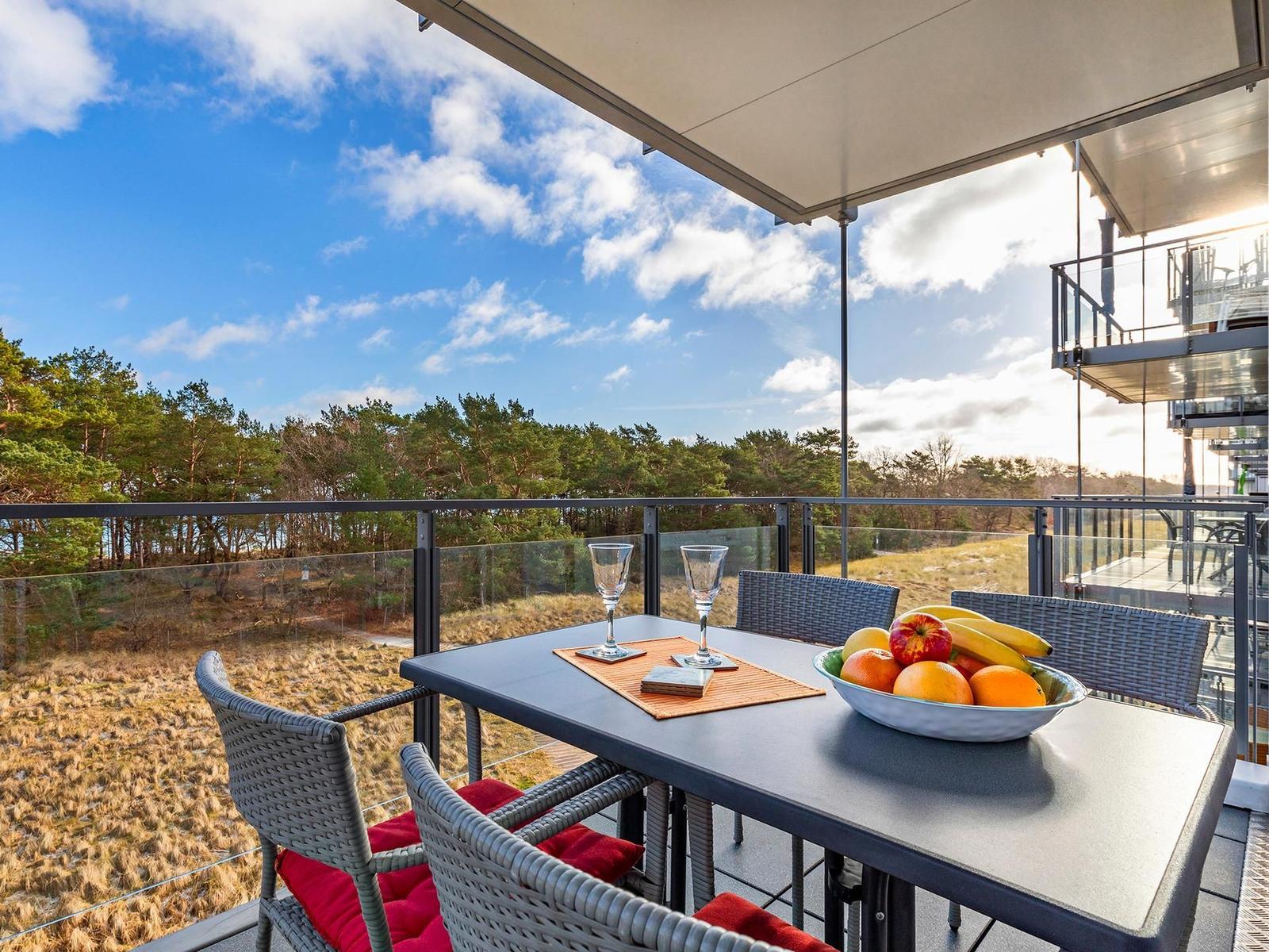 Terrasse mit Tisch, Stühlen und Obstschale. Blick auf Wald und Himmel.