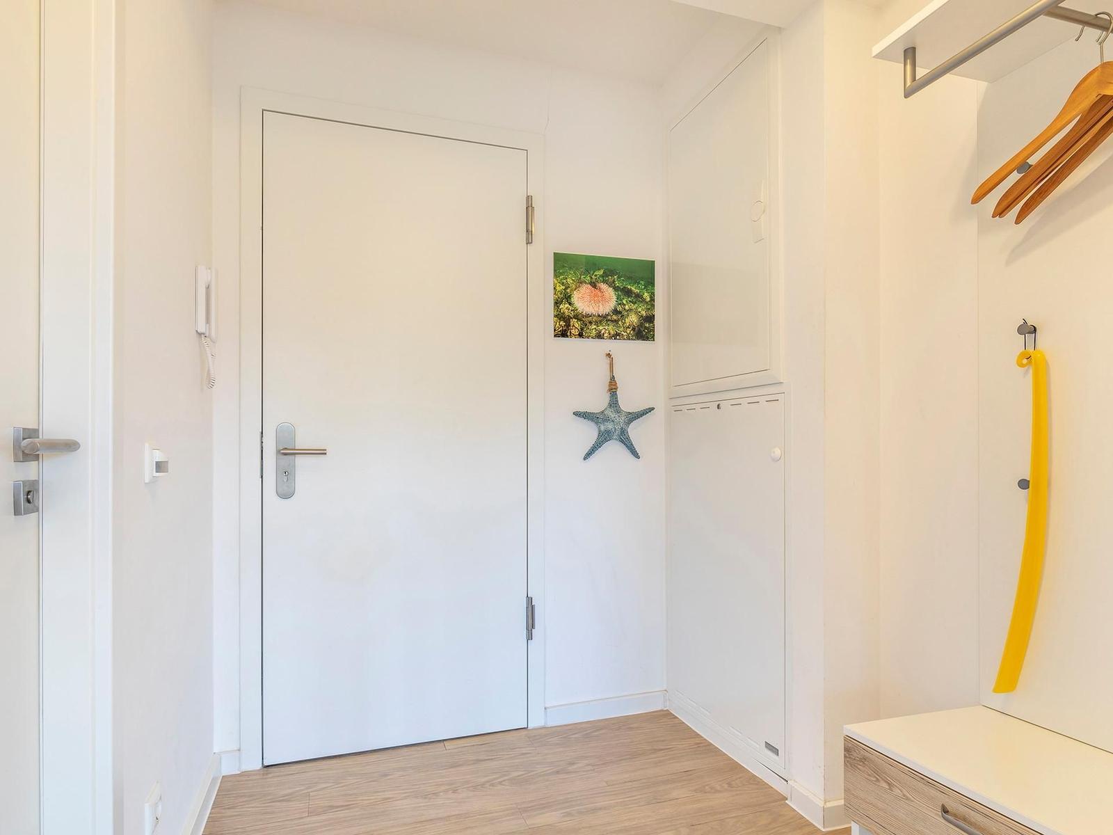 Eingangsbereich mit weißer Tür, Wandbild und Kleiderschrank mit Haken.